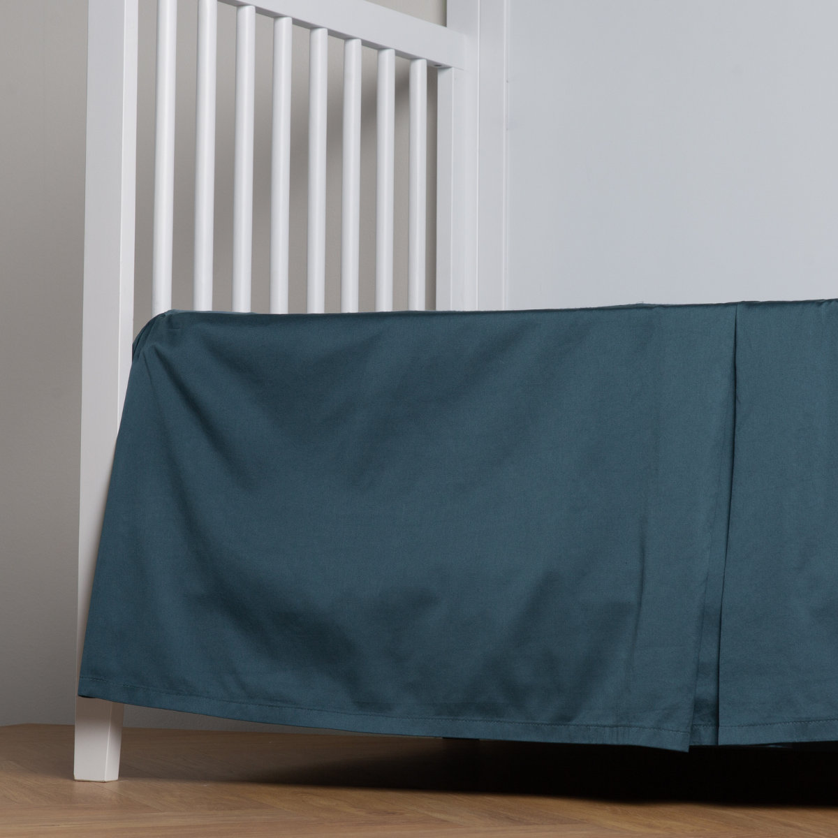 Midnight: cotton sateen cribi skirt with a center pleat shown straight on from a slight angle in a crib without a crib mattress.