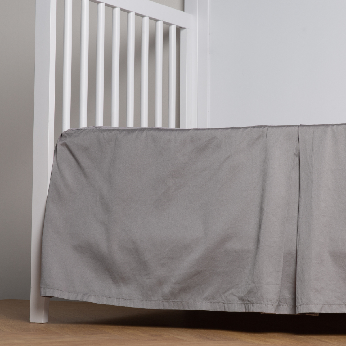 Moonlight: cotton sateen cribi skirt with a center pleat shown straight on from a slight angle in a crib without a crib mattress.