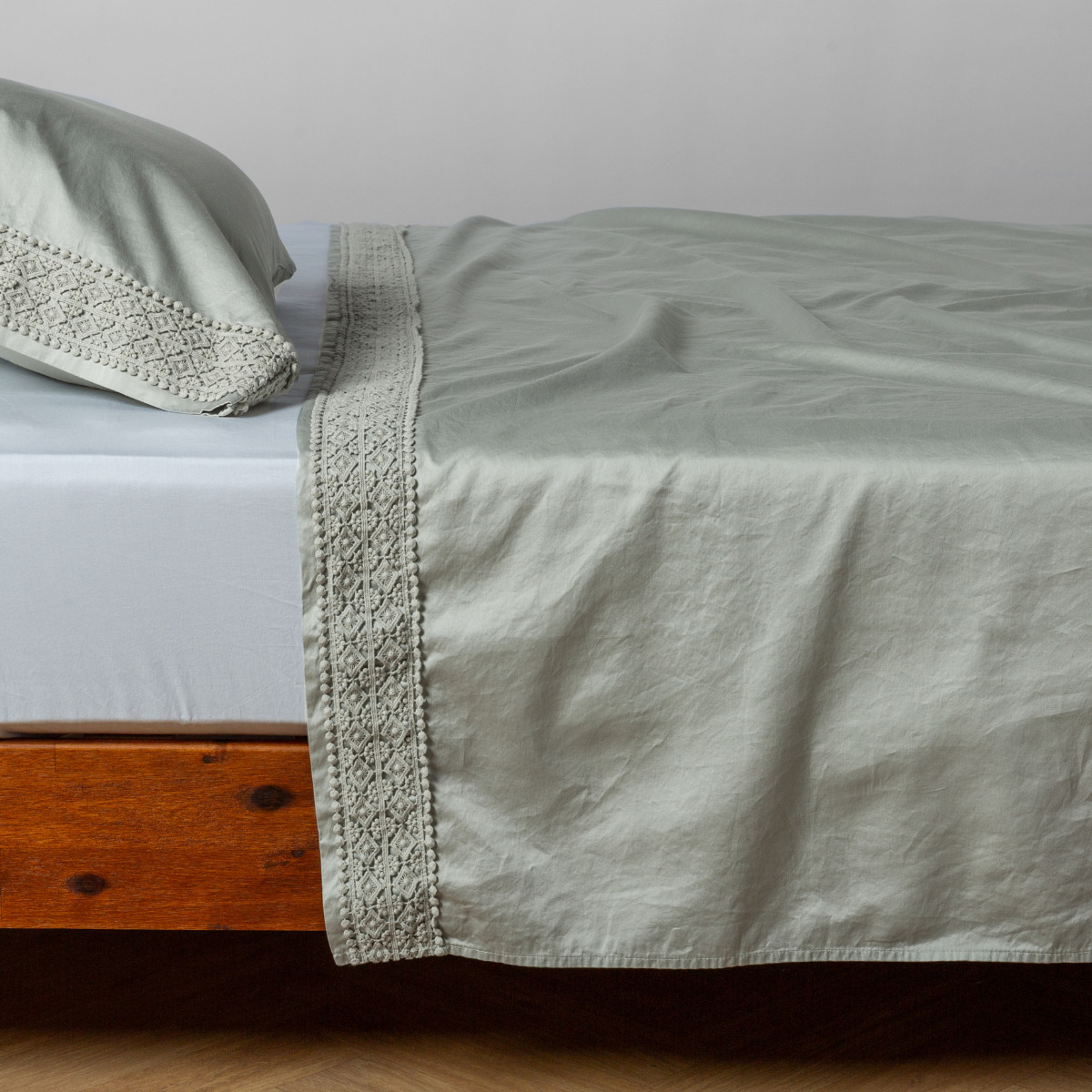 Matching lace trimmed cotton sateen flat sheet and pillowcase shown with a winter white fitted sheet - side view.