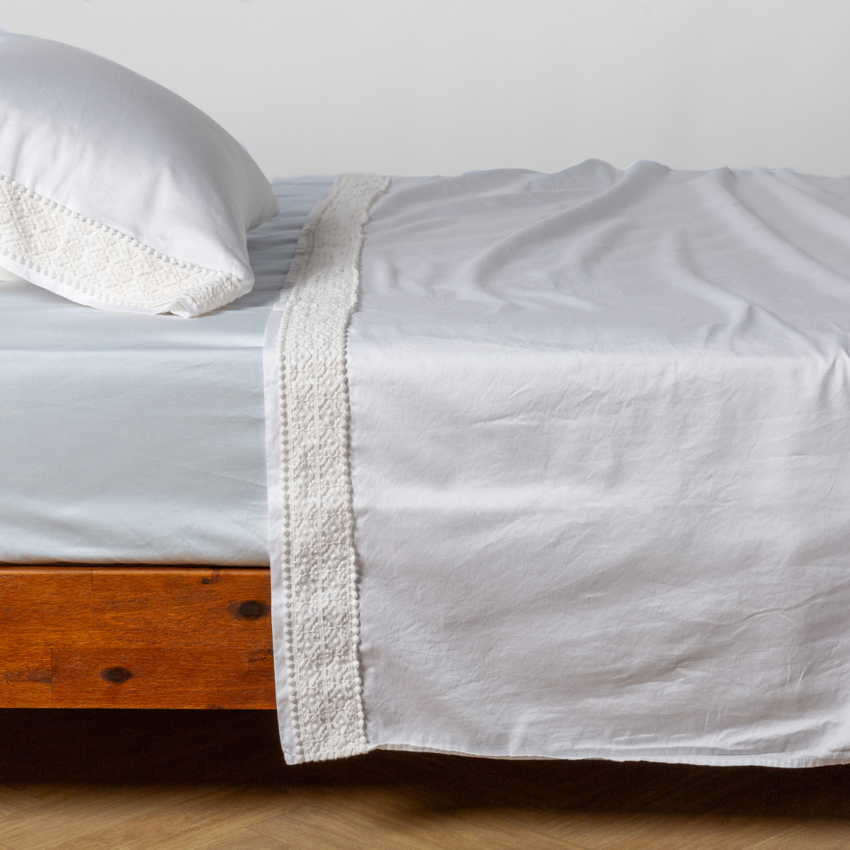 Matching lace trimmed cotton sateen flat sheet and pillowcase shown with a winter white fitted sheet - side view.