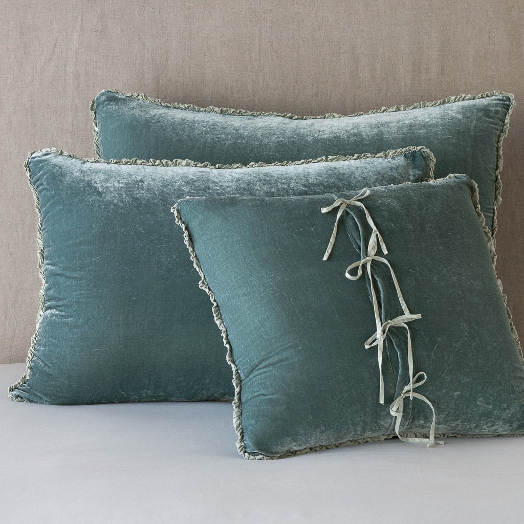 : Three carmen shams in eucalyptus leaning upright against a neutral headboard. The front sham is backwards, showcasing the charmeuse tie closures.
