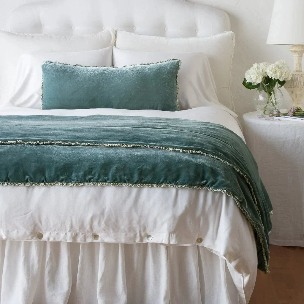 Eucalyptus: Silk velvet shams with a petite ruffle on a white bed, stacked behind sleeping and throw pillows - view from end of bed.