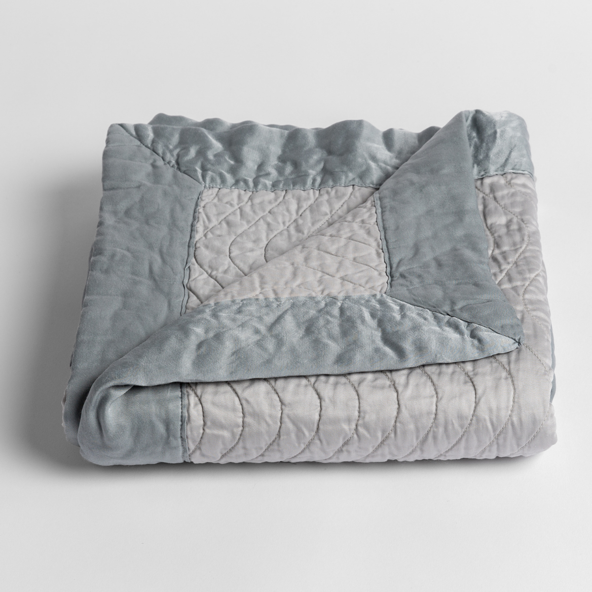 Mineral: a folded quilted cotton sateen baby blanket with its corner folded down to show the trim contrast - shot against a white background.