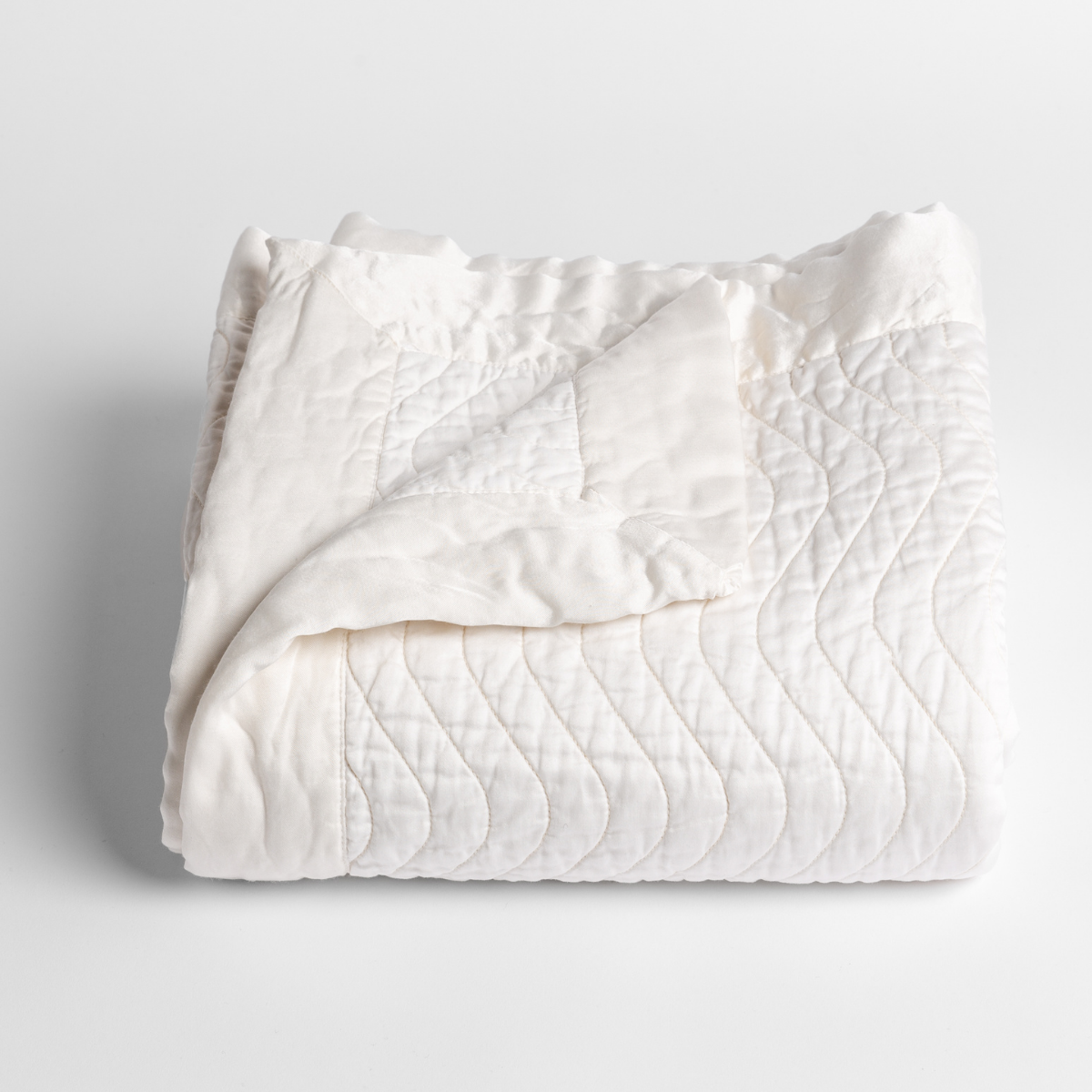 Winter White: a folded quilted cotton sateen baby blanket with its corner folded down to show the trim contrast - shot against a white background.