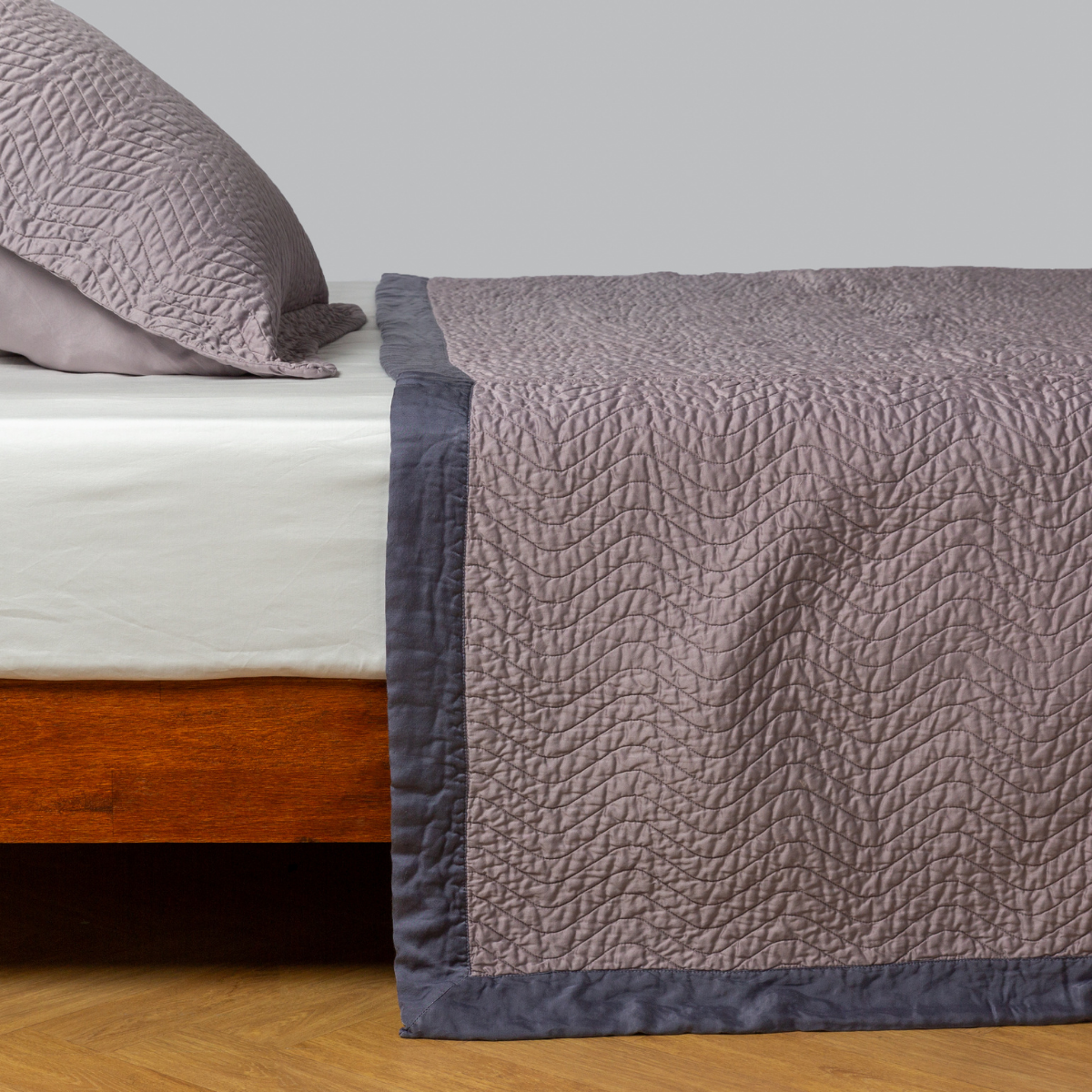 French Lavender: quilted cotton sateen coverlet with matching sham on a winter white fitted sheet - side view.