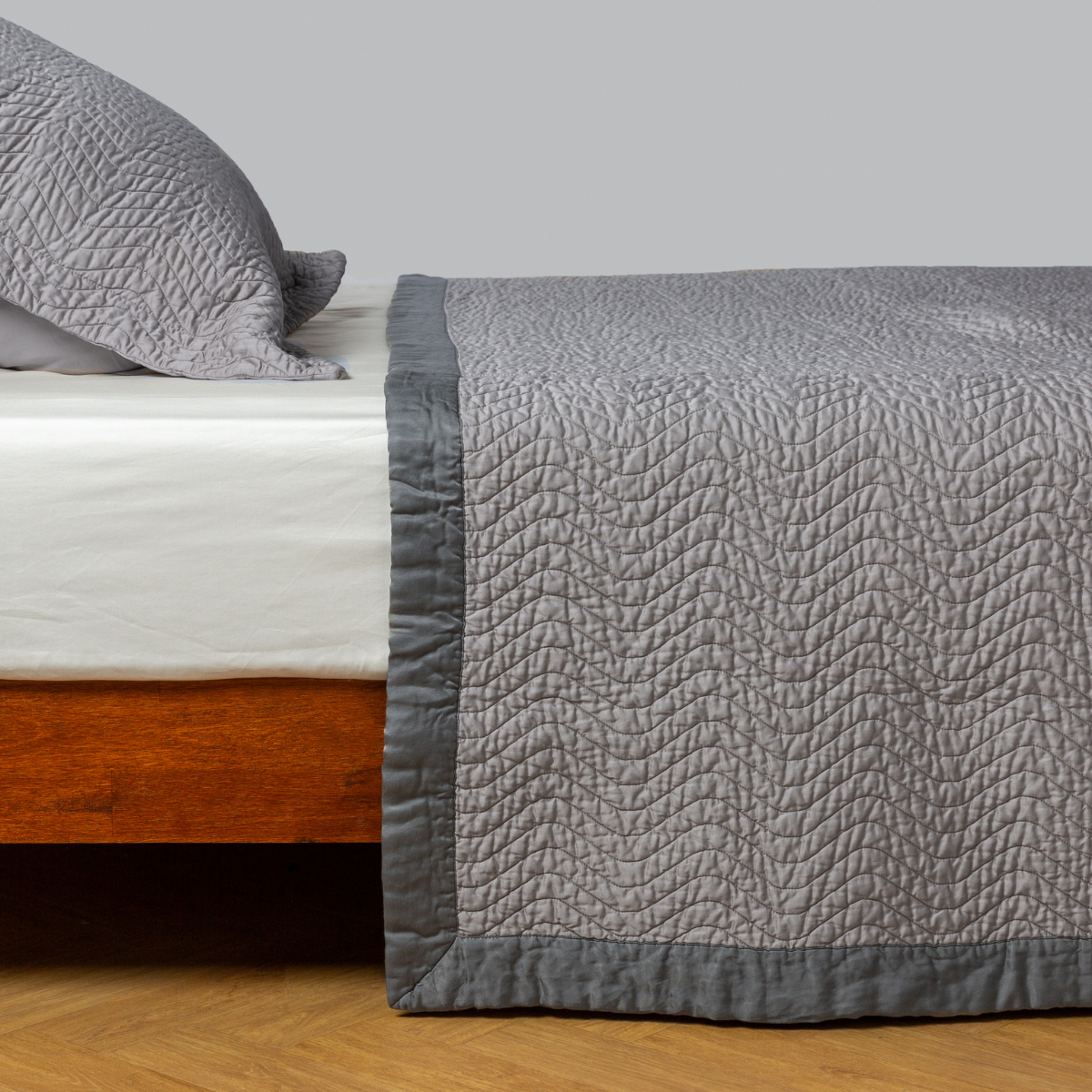 Moonlight: quilted cotton sateen coverlet with matching sham on a winter white fitted sheet - side view.