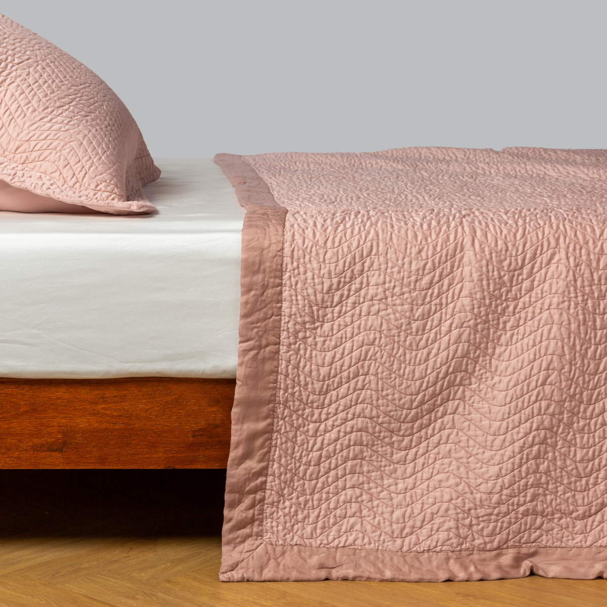 Rouge: quilted cotton sateen coverlet with matching sham on a winter white fitted sheet - side view.