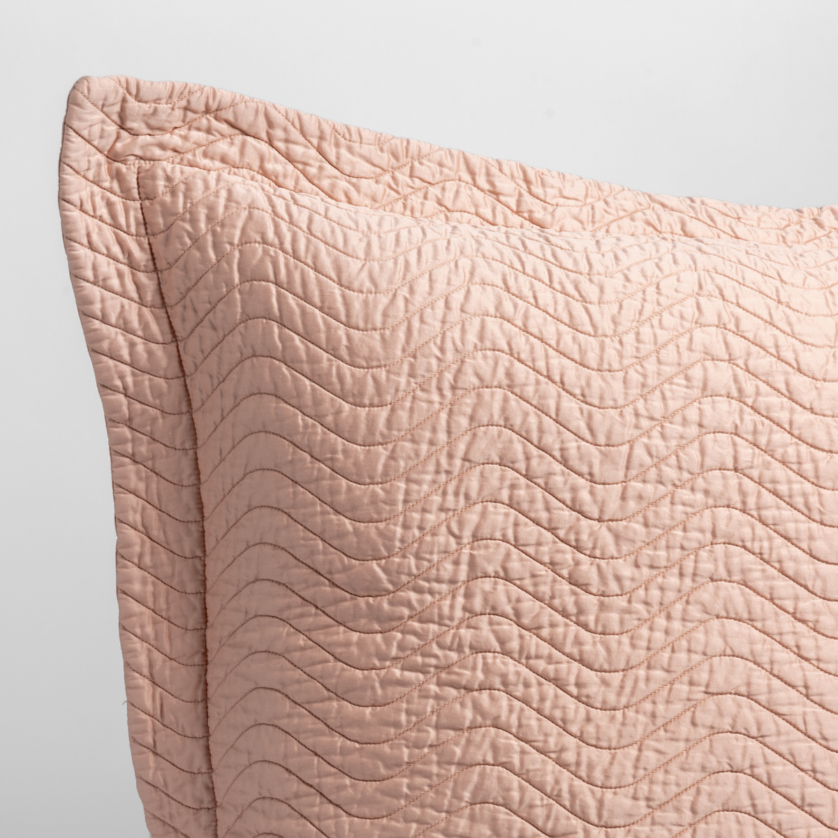 Rouge: a close up of a pillow corner showing the flange framing quilted cotton sateen shot against a white background.