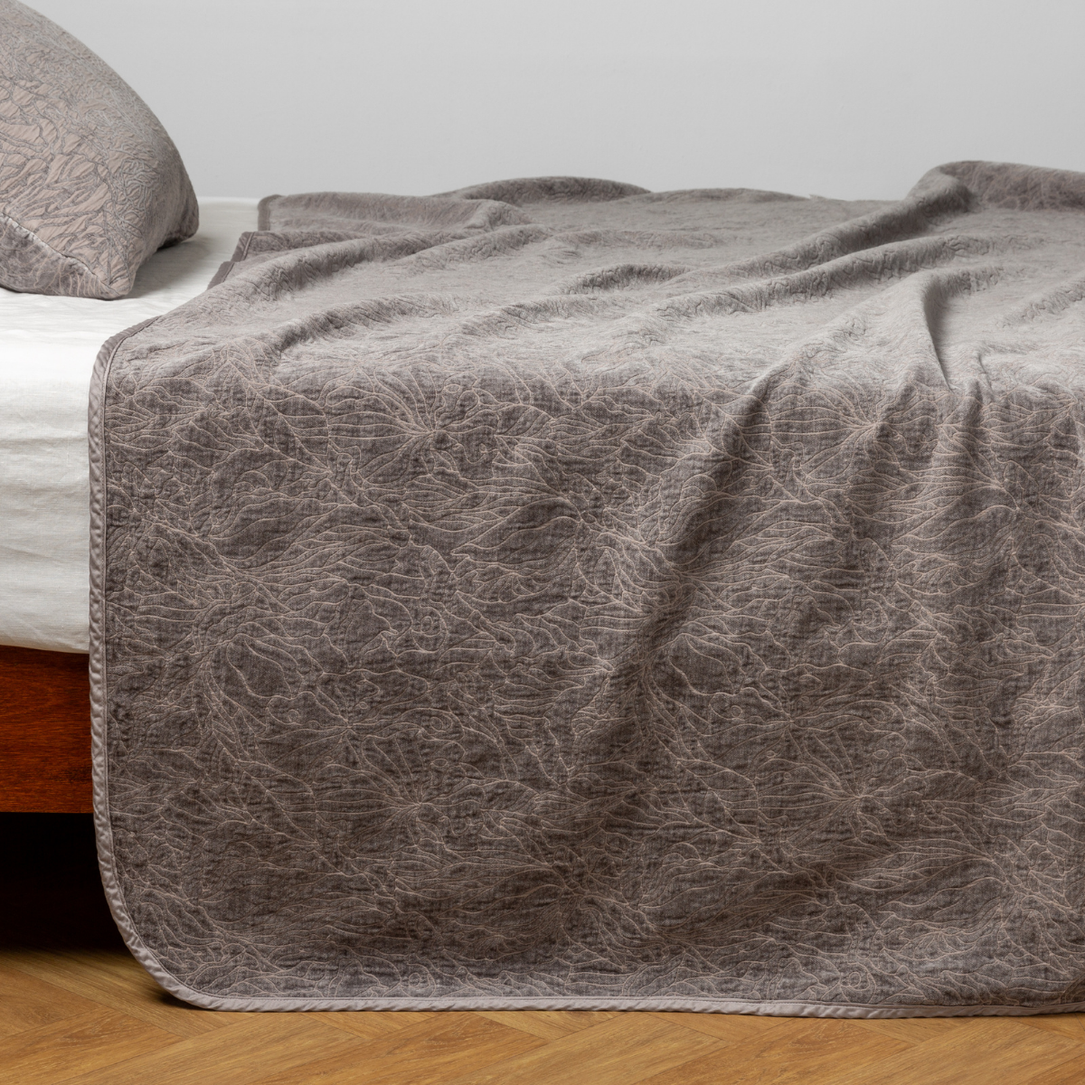 Moonlight: side view of the chenille jacquard side of a bedspread with the cotton jacquard side showing on the matching sham — shown with a winter white fitted sheet.