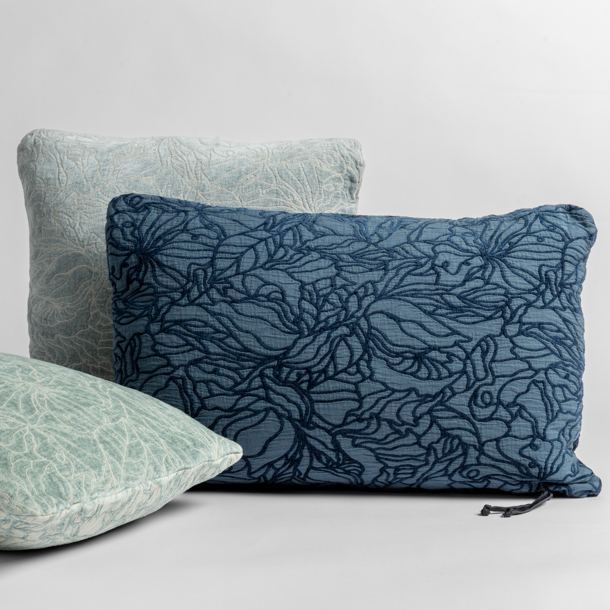 : throw pillows in different sizes and shapes shown in green and blue tones, the different sides of the pillow show the tonal and pattern contrast.