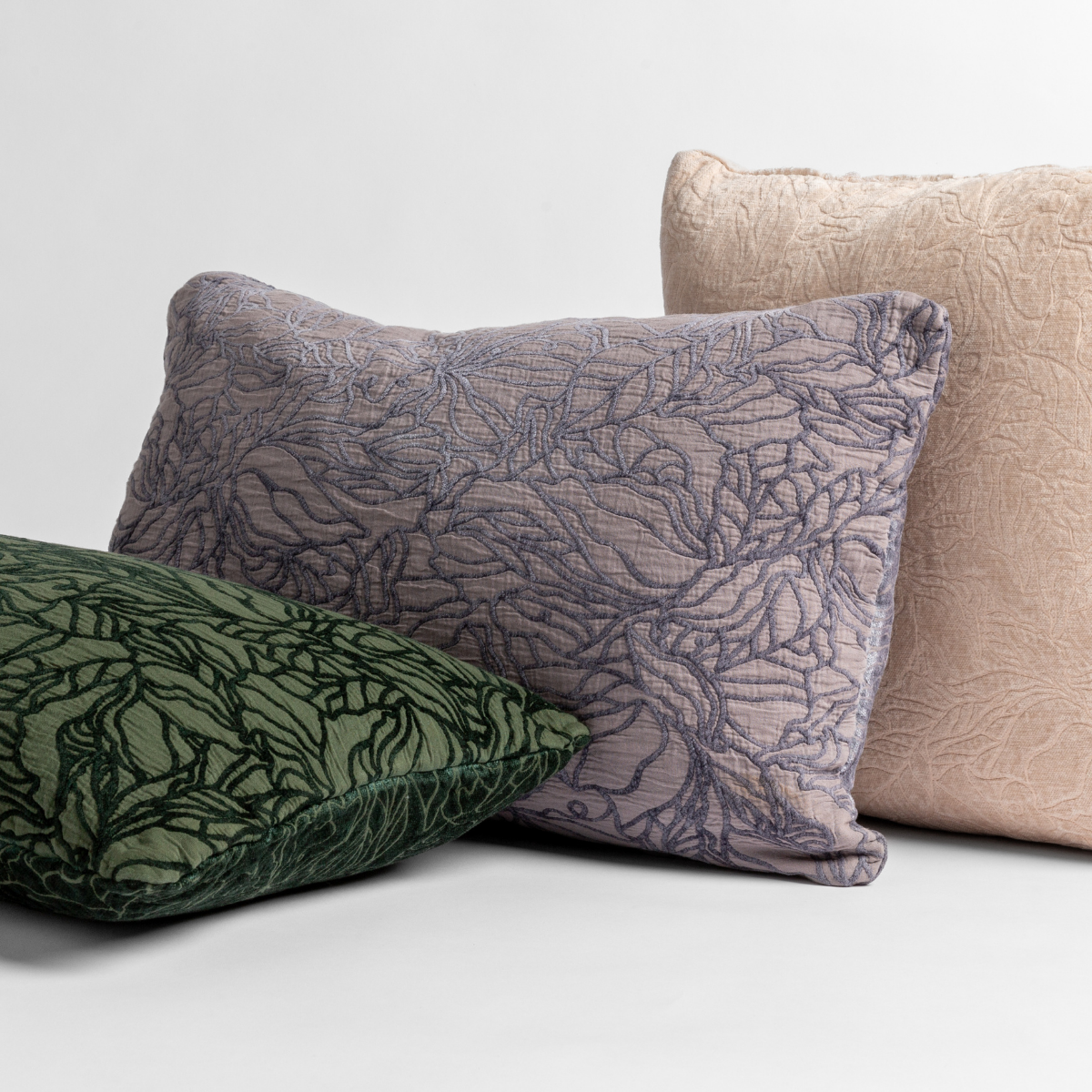 three throw pillows shown leaning against one another, in different colors with different sides showing their cotton jacquard and chenille jacquard faces - shown against a white background.
