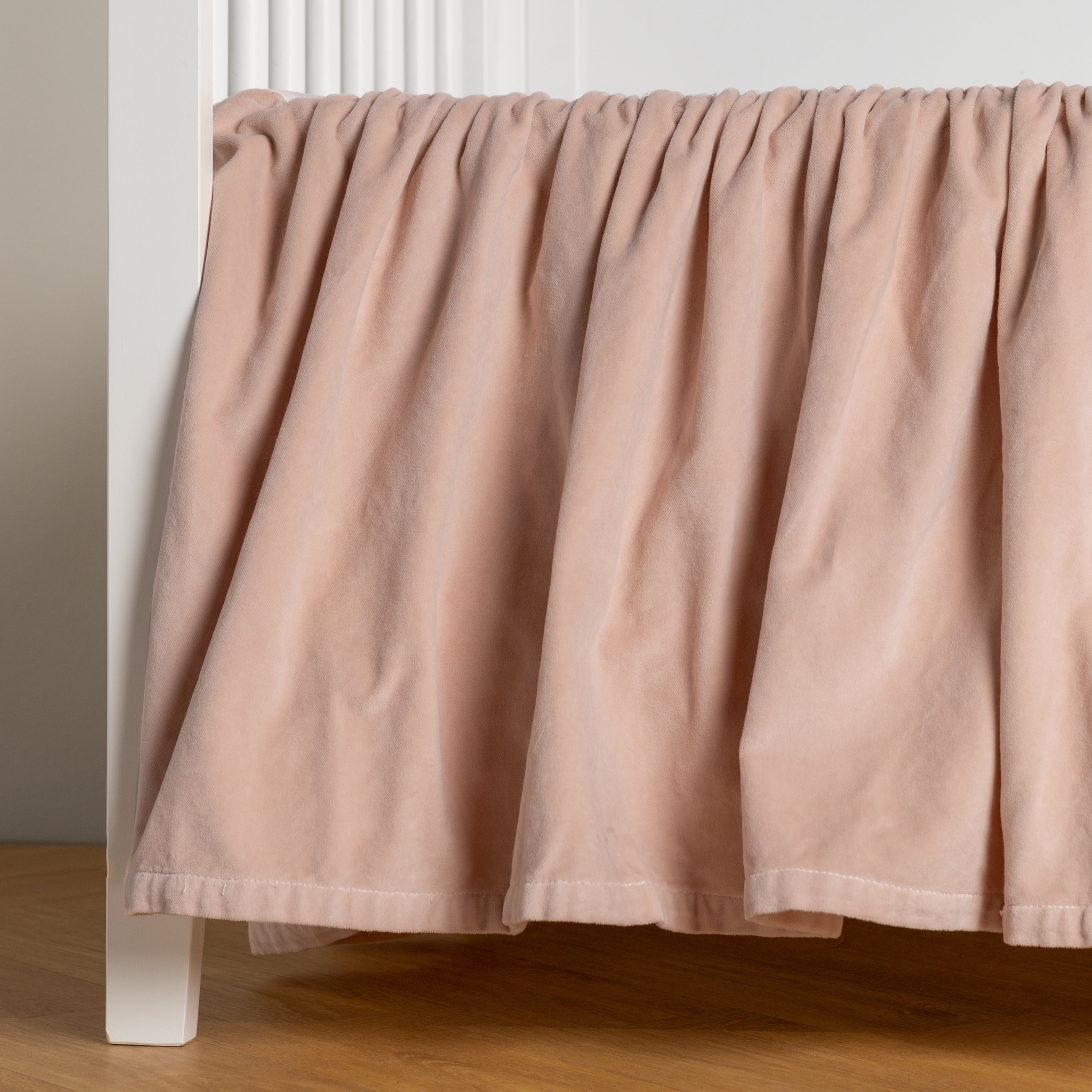 Pearl: cotton velvet crib skirt shown on a white crib .
