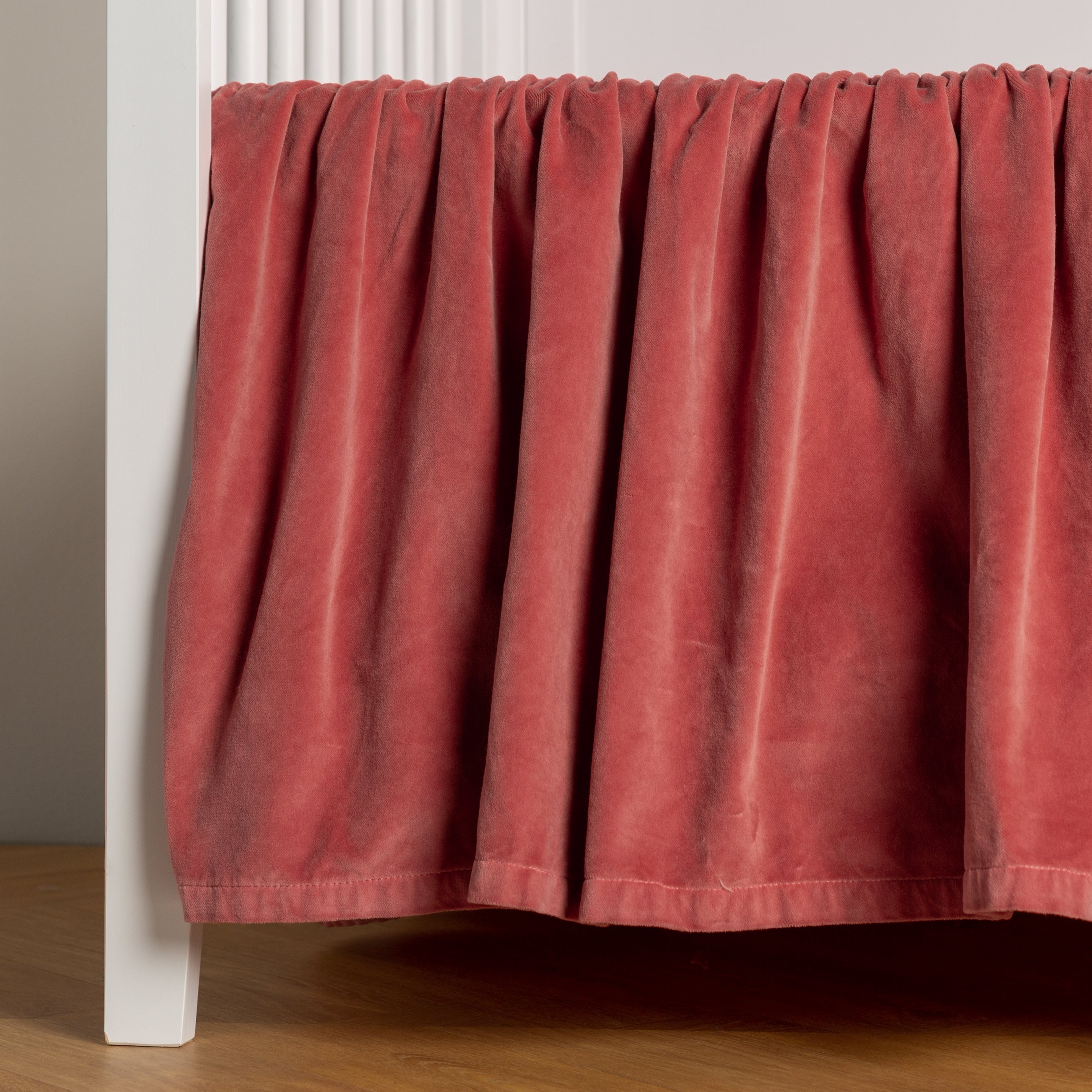 Poppy: cotton velvet crib skirt shown on a white crib .