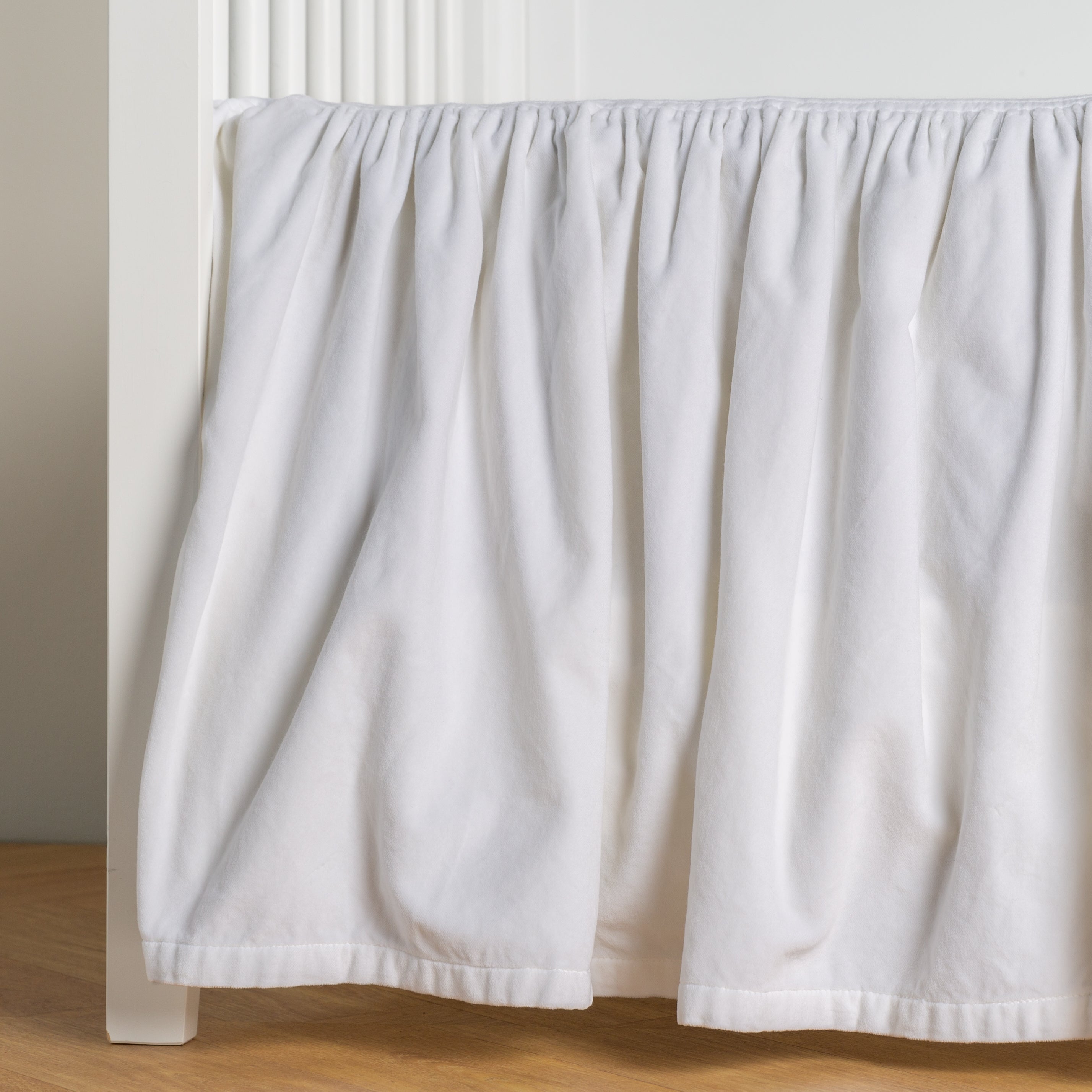 White: cotton velvet crib skirt shown on a white crib .
