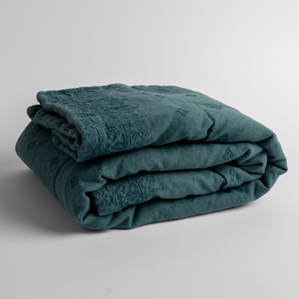 Cenote: embroidered linen baby blanket folded and shown overhead from a slight angle against a white background.