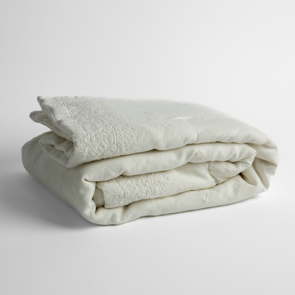 Winter White: embroidered linen baby blanket folded and shown overhead from a slight angle against a white background.