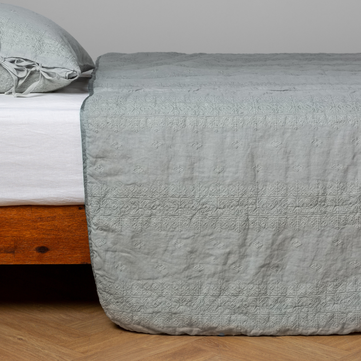 Eucalyptus: embroidered midweight linen bedspread with matching sham on a bed with a white fitted sheet. Shot from the side view, the bedframe is slightly visible against a white background and medium wood floor.