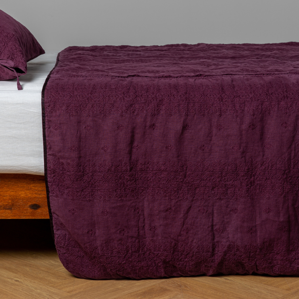 Fig: embroidered midweight linen bedspread with matching sham on a bed with a white fitted sheet. Shot from the side view, the bedframe is slightly visible against a white background and medium wood floor.