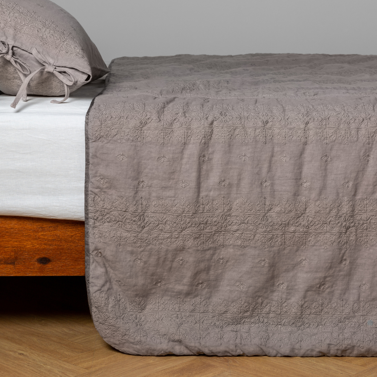 Fog: embroidered midweight linen bedspread with matching sham on a bed with a white fitted sheet. Shot from the side view, the bedframe is slightly visible against a white background and medium wood floor.