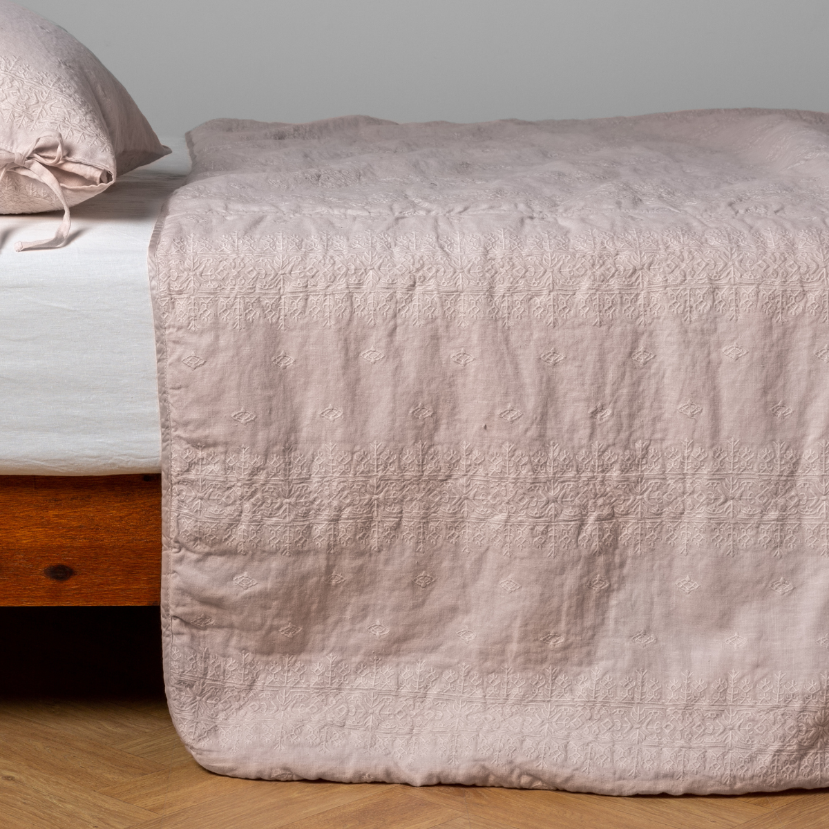 Pearl: embroidered midweight linen bedspread with matching sham on a bed with a white fitted sheet. Shot from the side view, the bedframe is slightly visible against a white background and medium wood floor.