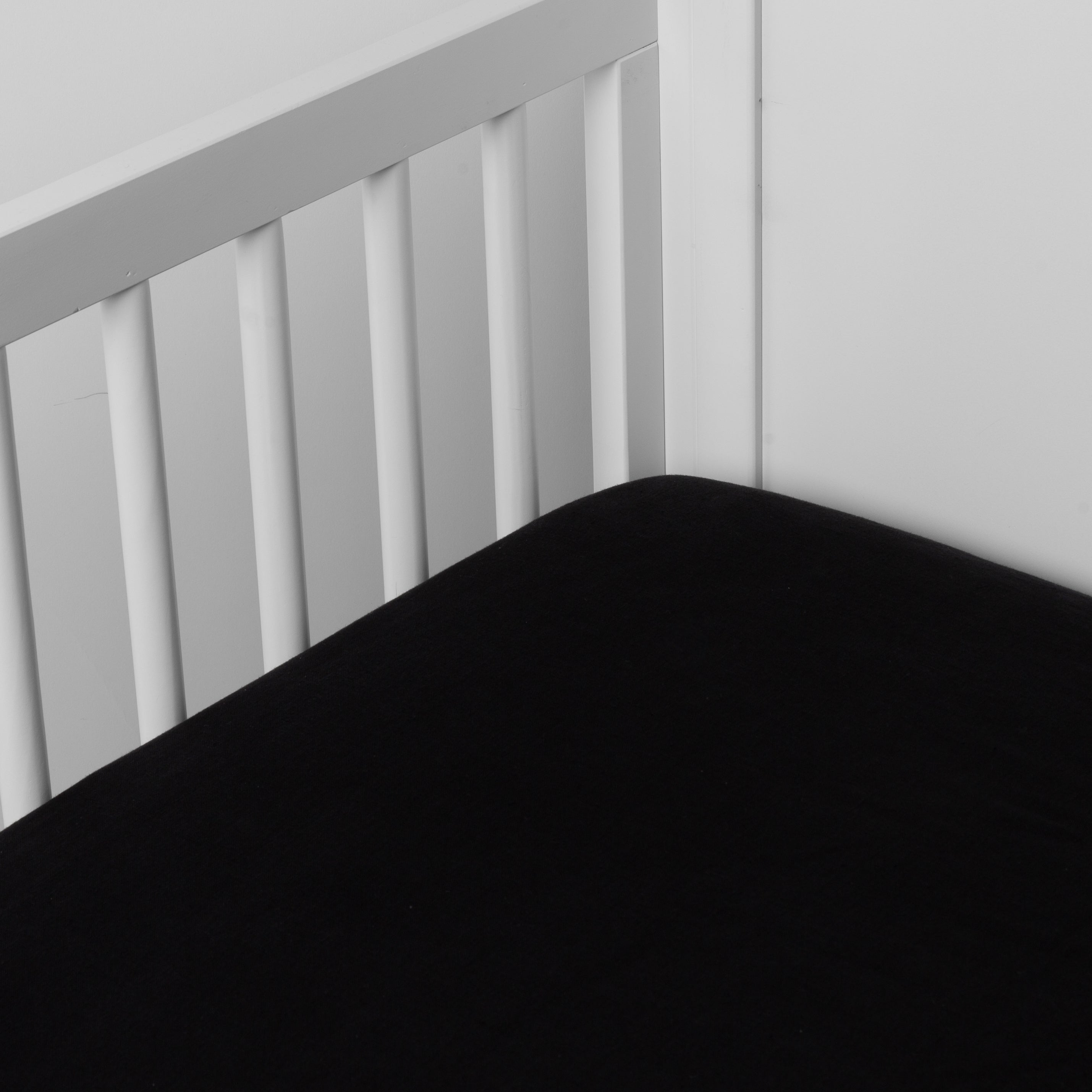 Corvino: linen crib sheet on the mattress shot slightly overhead into the corner of a white crib. against a white background.