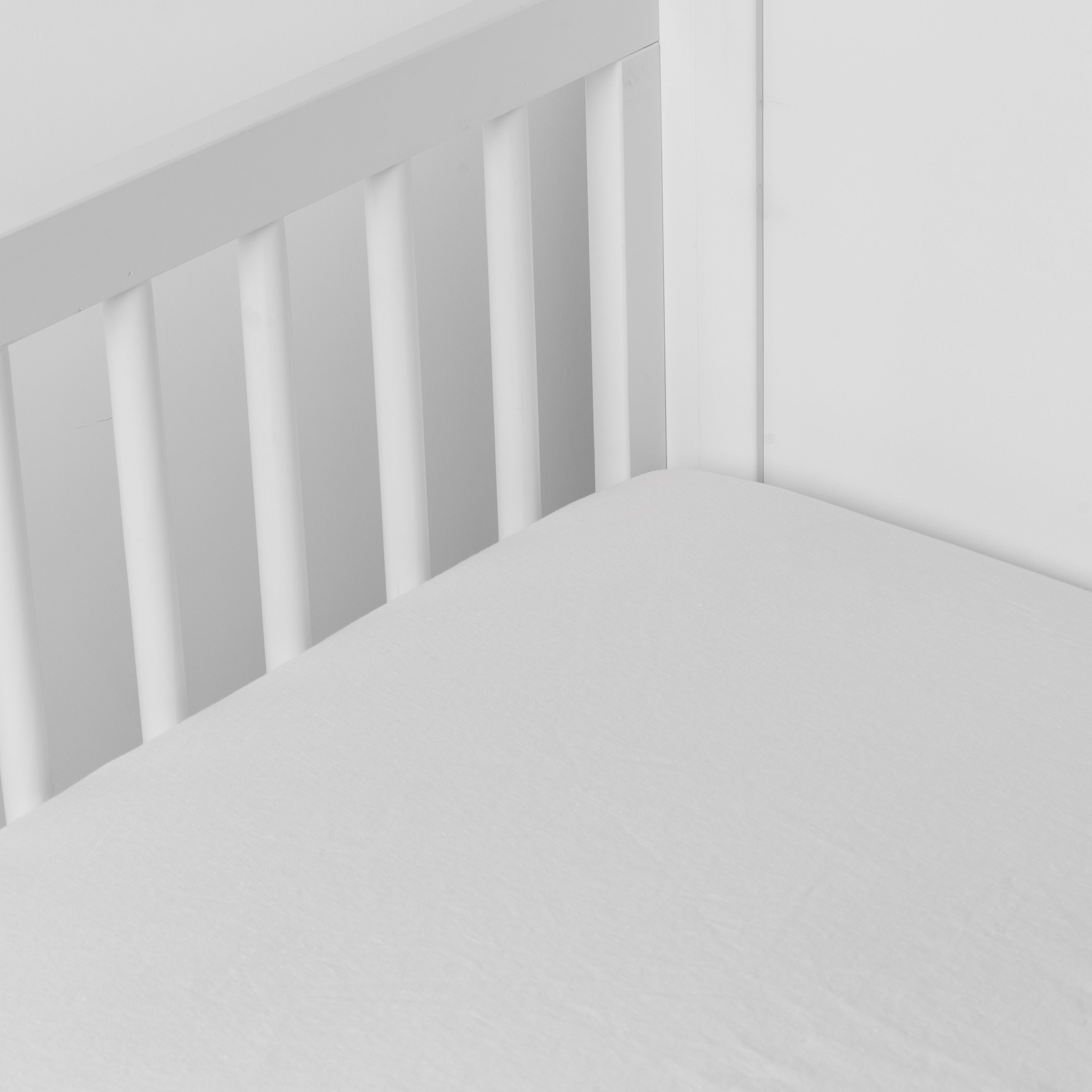 Winter White: linen crib sheet on the mattress shot slightly overhead into the corner of a white crib. against a white background.