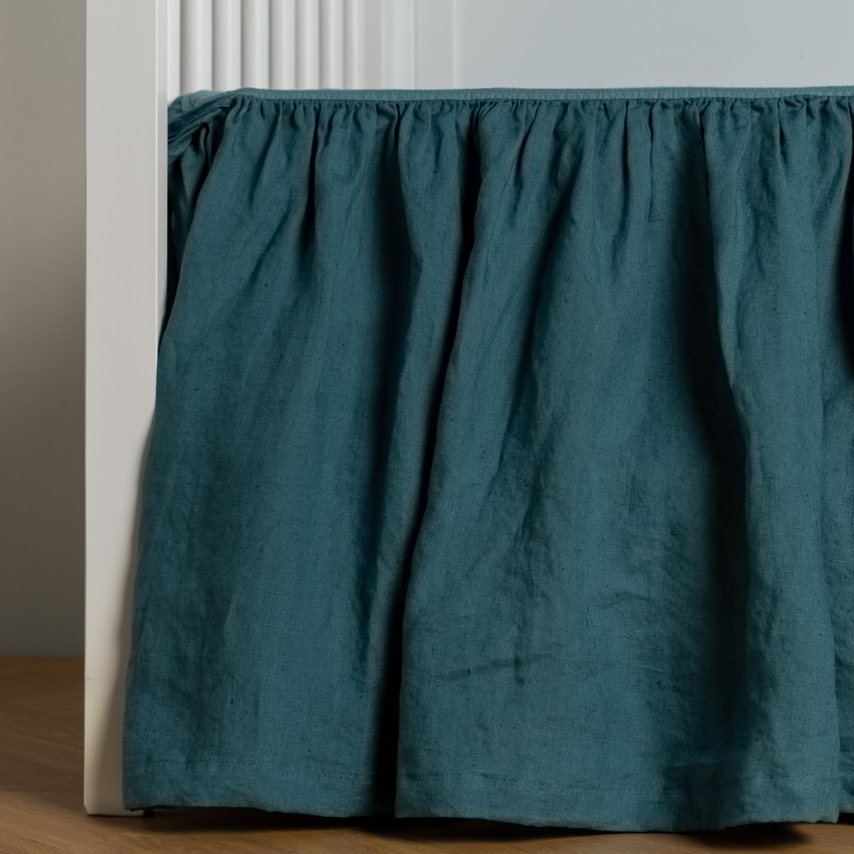 Cenote: crib skirt shown on a white crib with no mattress against a white wall and medium wood flooring.