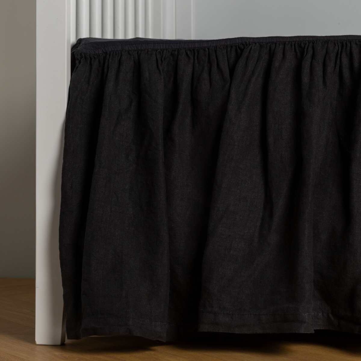 Corvino: crib skirt shown on a white crib with no mattress against a white wall and medium wood flooring.
