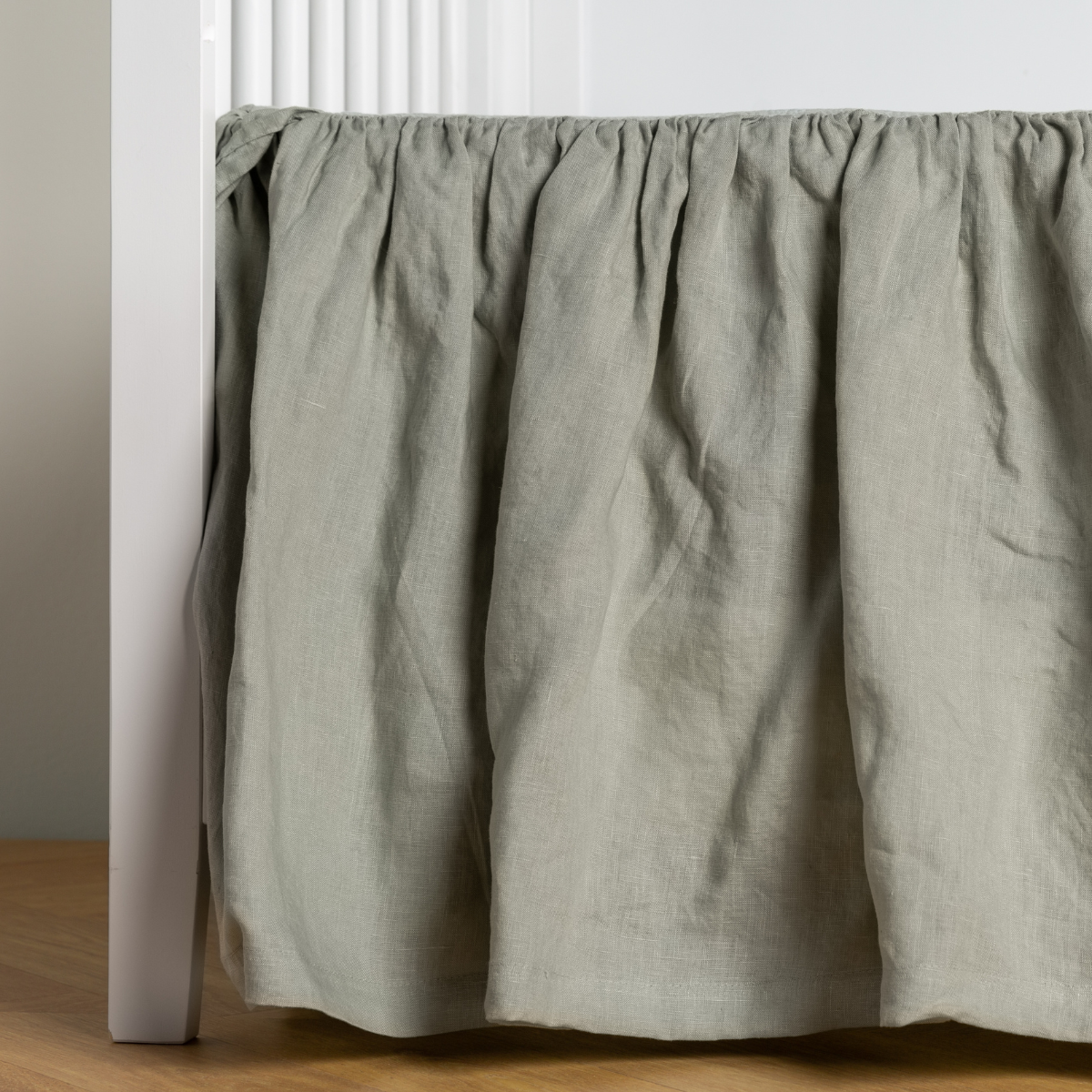 Eucalyptus: crib skirt shown on a white crib with no mattress against a white wall and medium wood flooring.