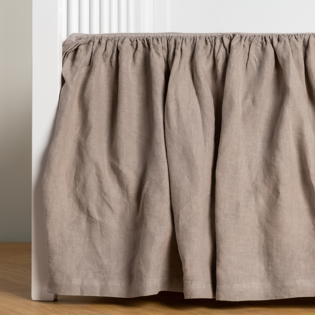 Fog: crib skirt shown on a white crib with no mattress against a white wall and medium wood flooring.