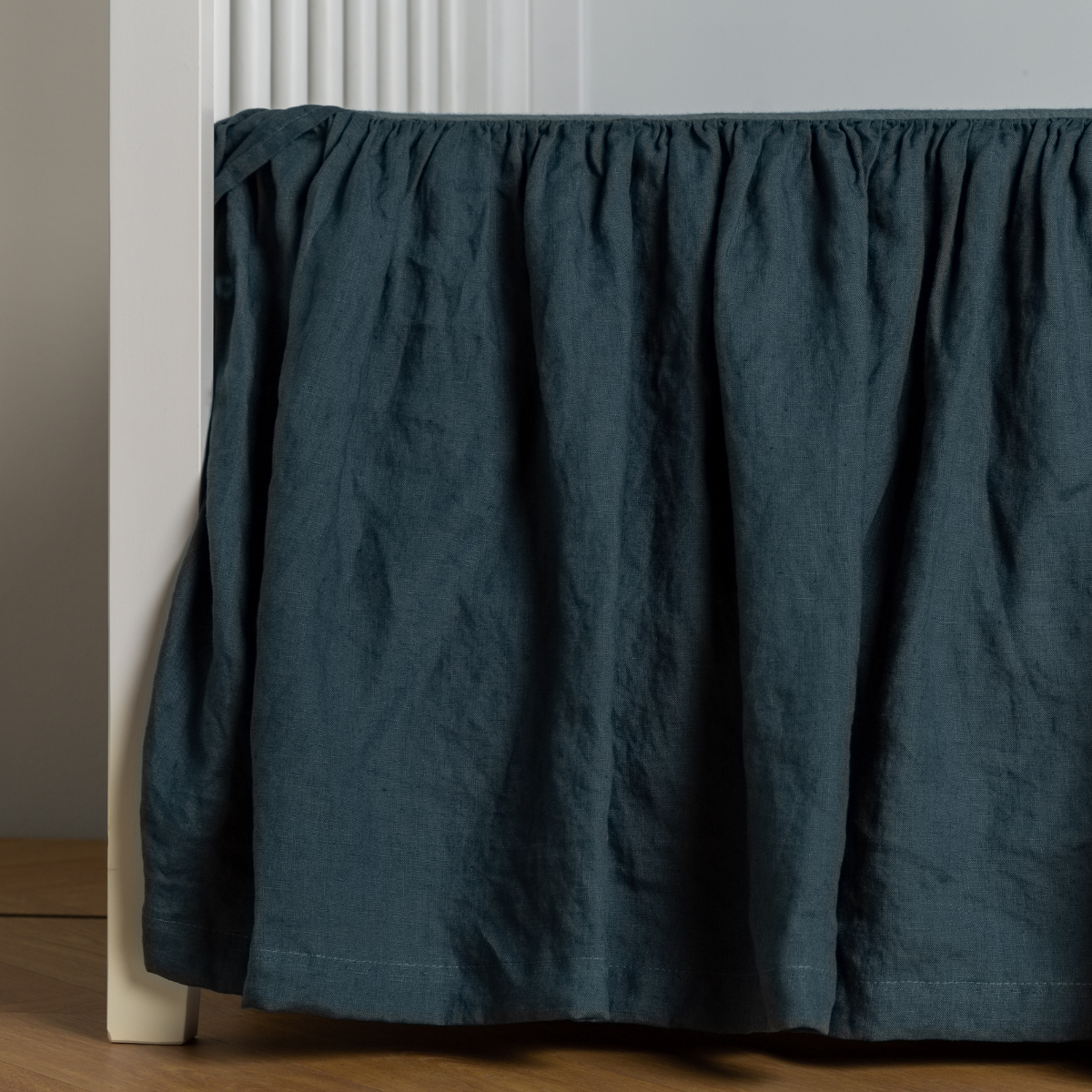 Midnight: crib skirt shown on a white crib with no mattress against a white wall and medium wood flooring.