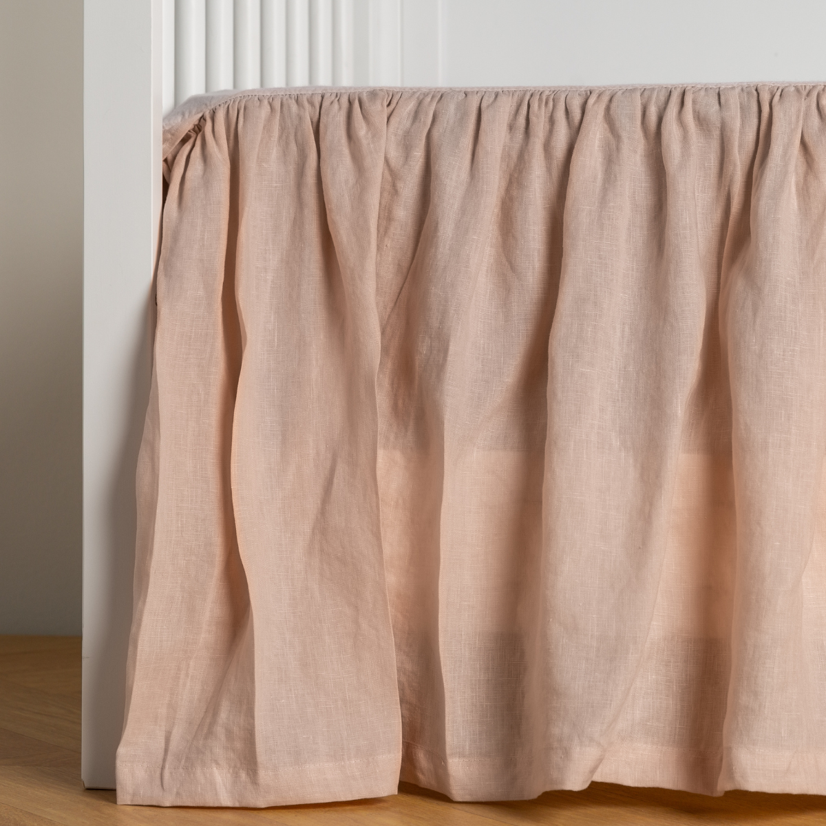 Pearl: crib skirt shown on a white crib with no mattress against a white wall and medium wood flooring.