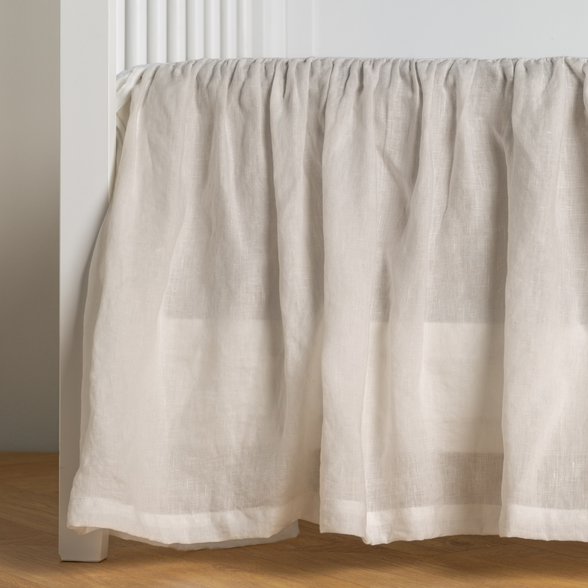 Winter White: crib skirt shown on a white crib with no mattress against a white wall and medium wood flooring.