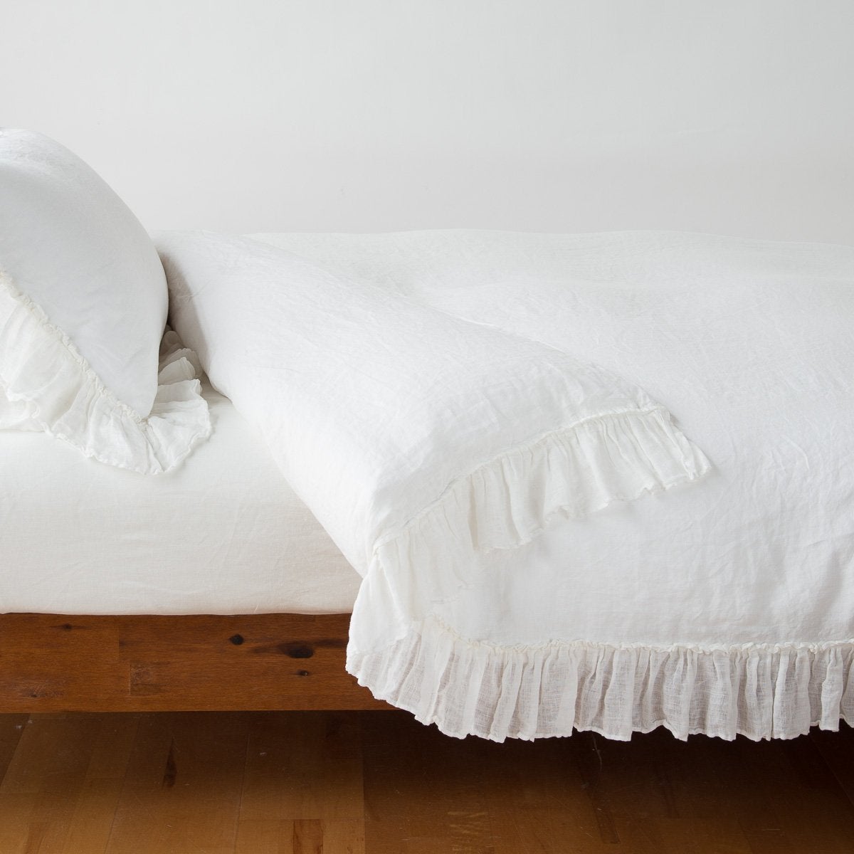 : Linen Whisper duvet cover folded back over a white fitted sheet, shown with matching sham against a plain background - winter white, side view.