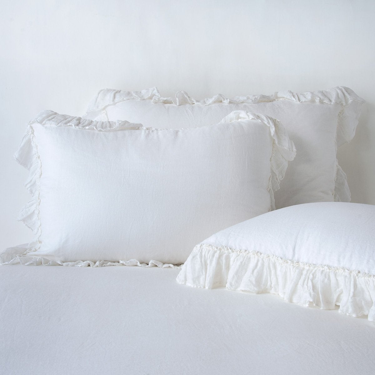 White: two shams leaning upright and one laying flat at an angle in the foreground, against a blank background.