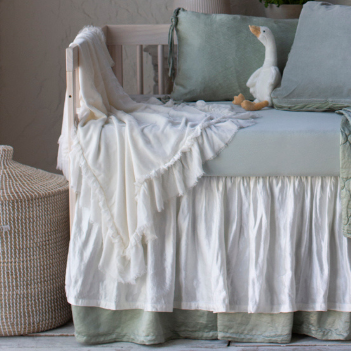 : Silk velvet blanket in winter white, draped over the front and side of a crib with soft green and white bedding.