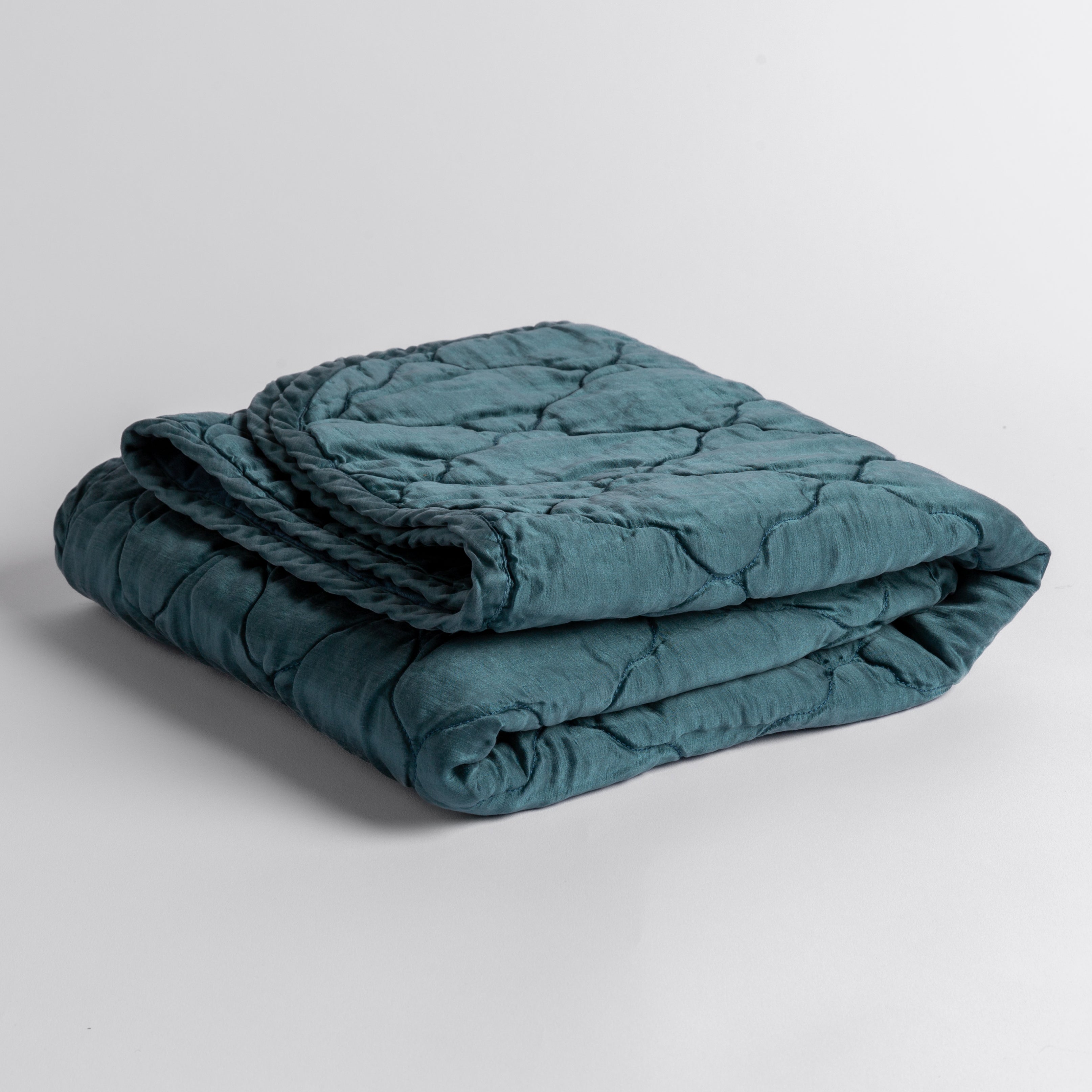 Cenote: quilted charmeuse blanket folded and shown against a white background from a slight overhead angle.