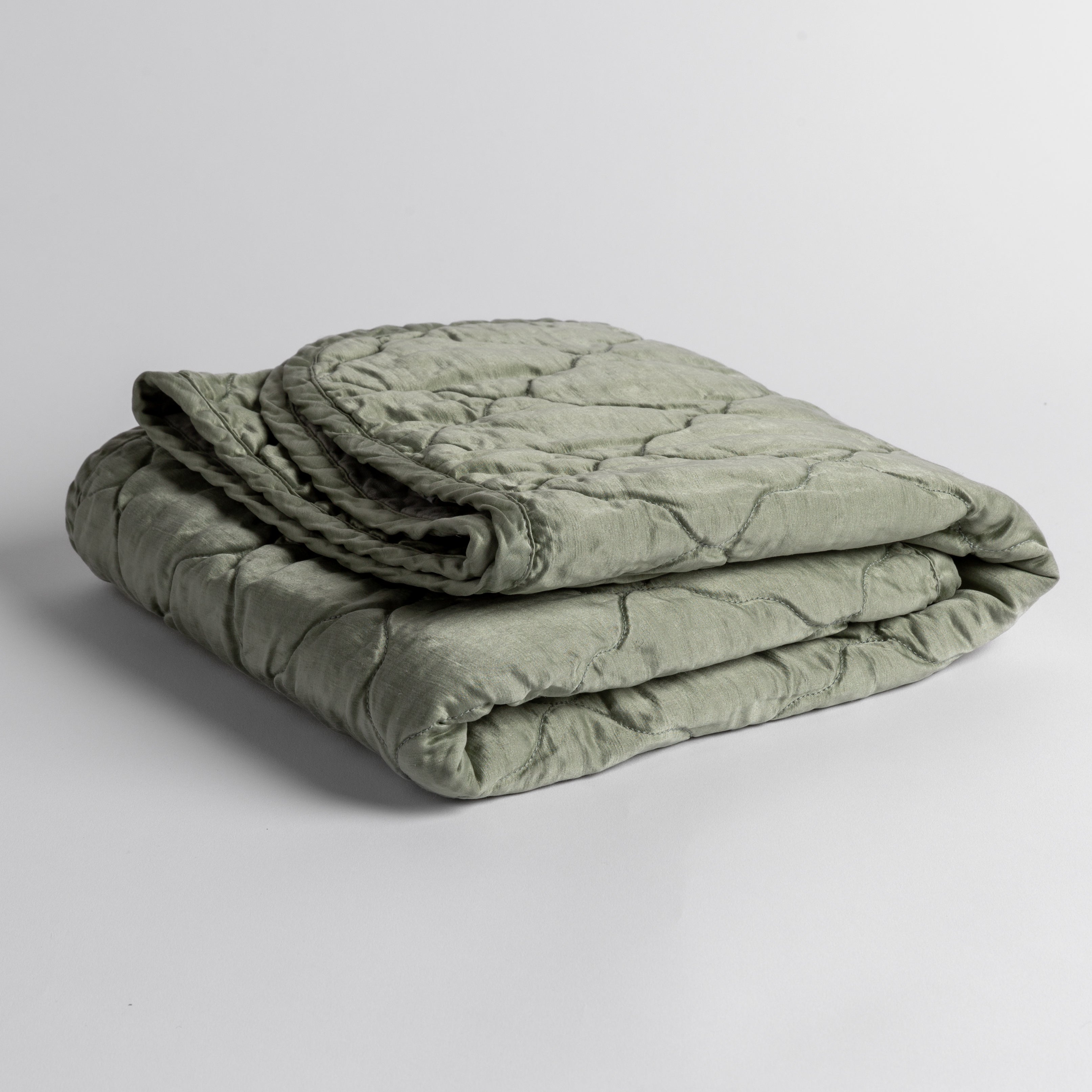 Eucalyptus: quilted charmeuse blanket folded and shown against a white background from a slight overhead angle.