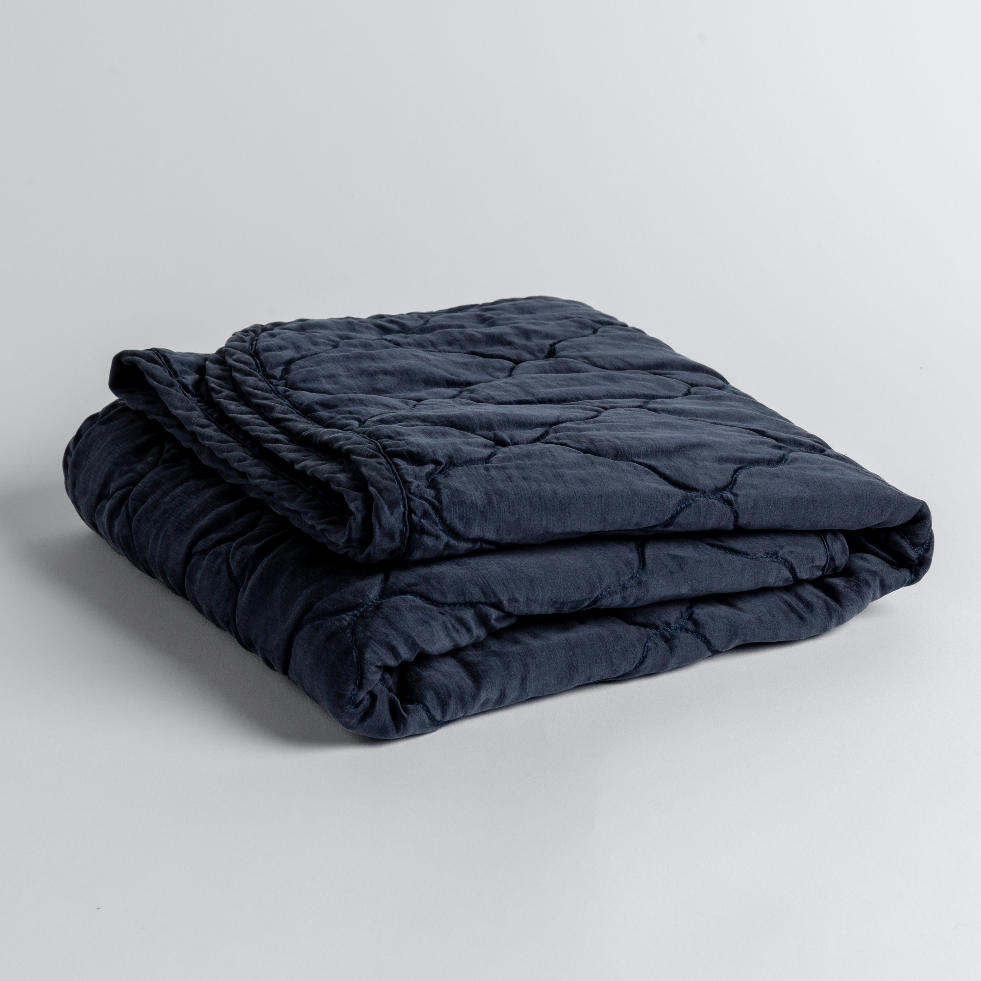 Midnight: quilted charmeuse blanket folded and shown against a white background from a slight overhead angle.