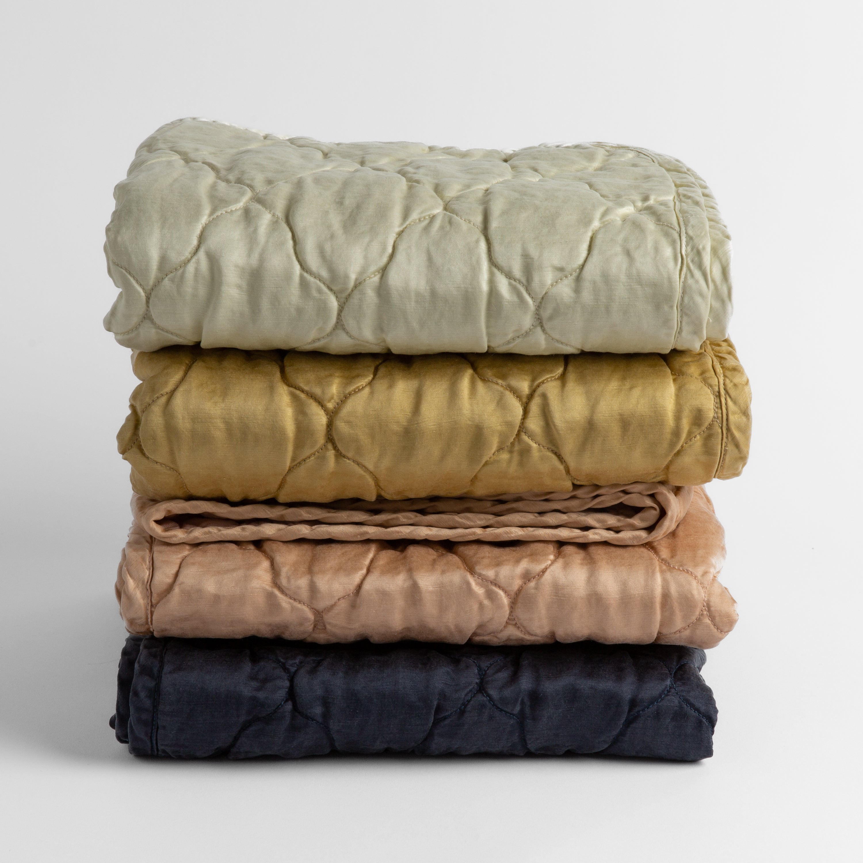 A stack of four quilted silk charmeuse baby blankets shown straight on against a white background. Blankets shown in Fog, Honeycomb, Rouge and Midnight