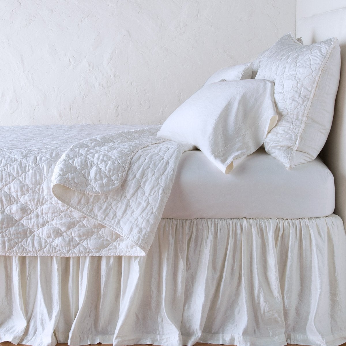White: shams with a matching coverlet pulled back over monochromatic sheeting - side view.