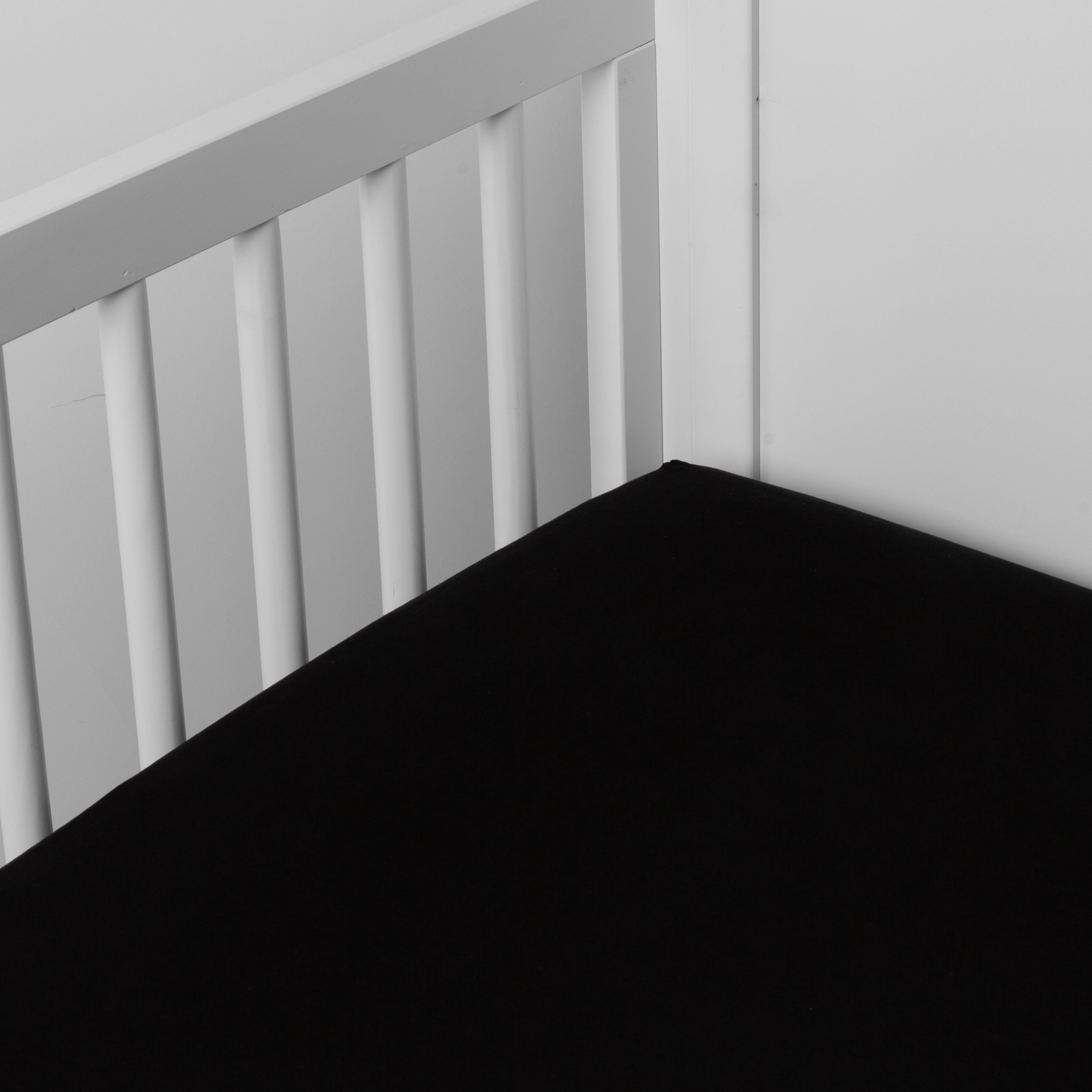 Corvino: crib sheet shown on a mattress shown from overhead into the corner of a crib.