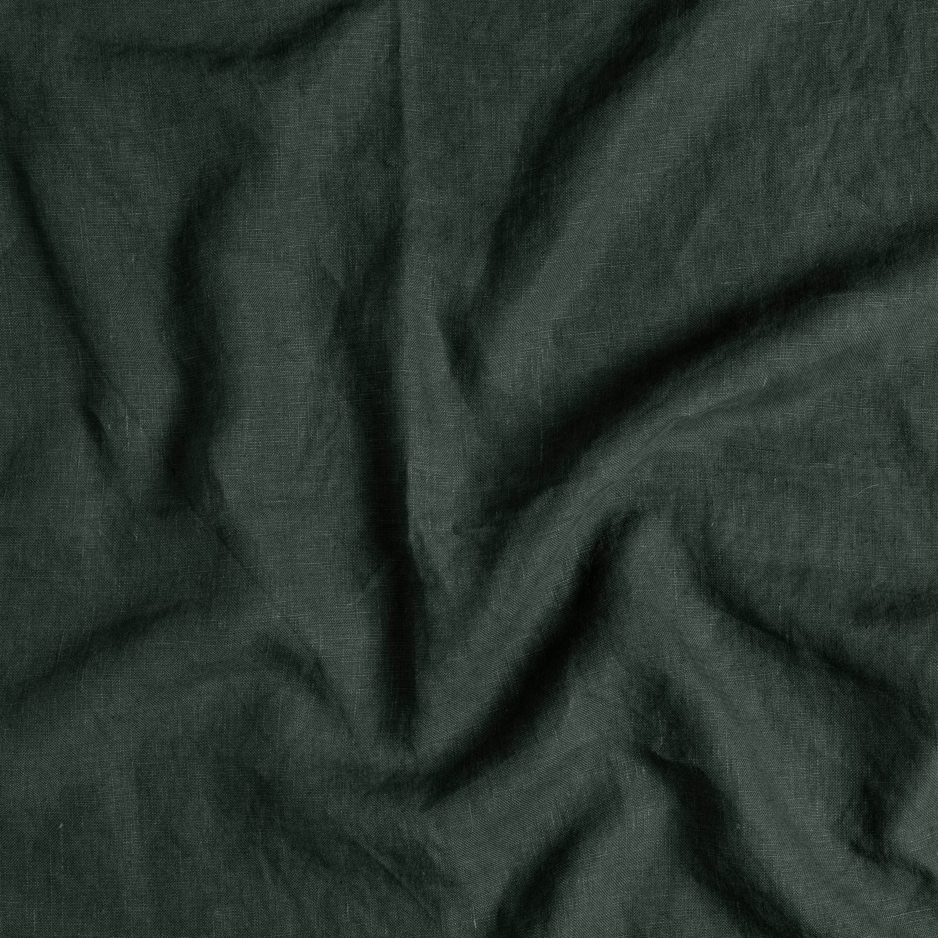A close up of midweight linen fabric gently rumpled in juniper, a dark green tone.