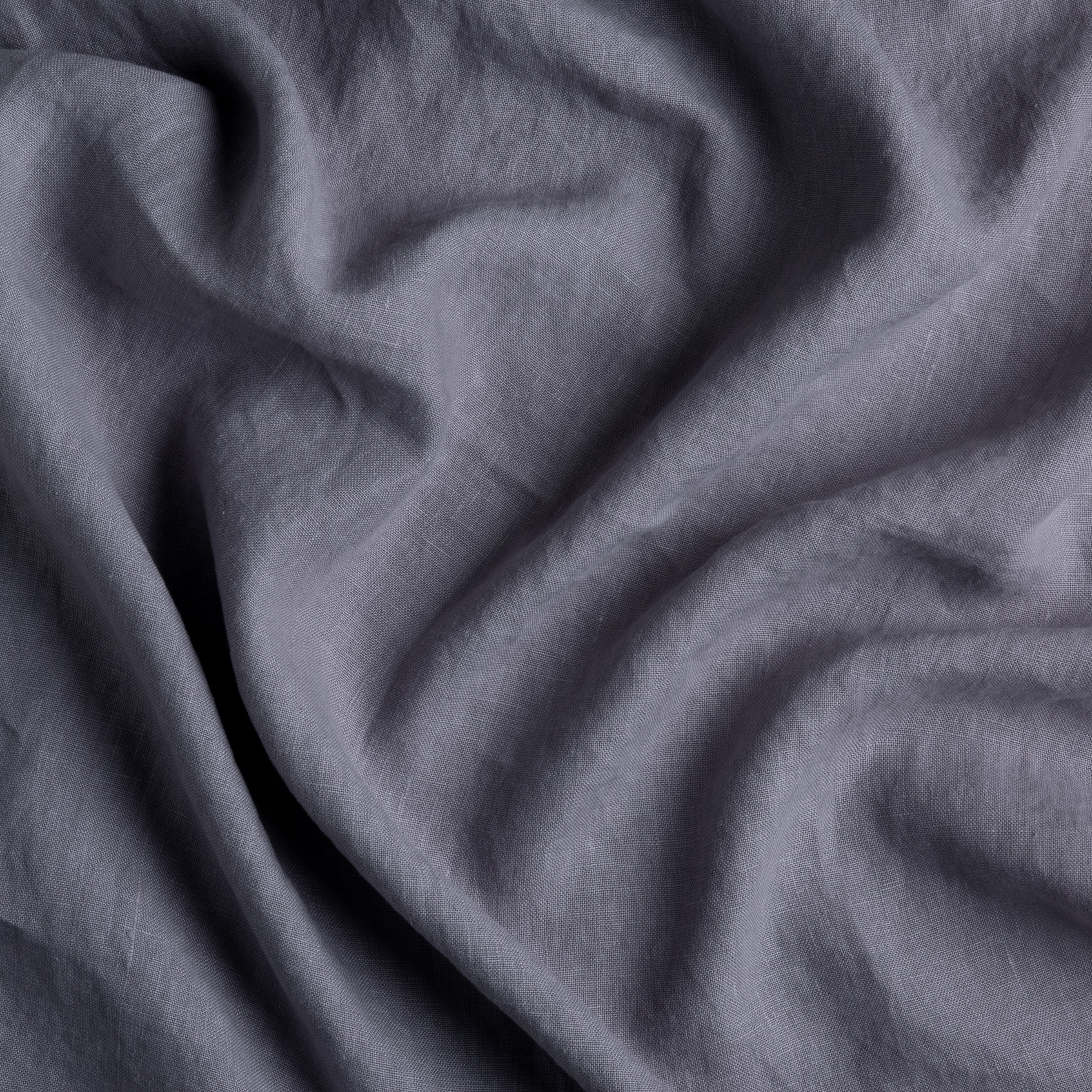 A close up of gently rumpled midweight linen in French Lavender, a neutral light purple tone.