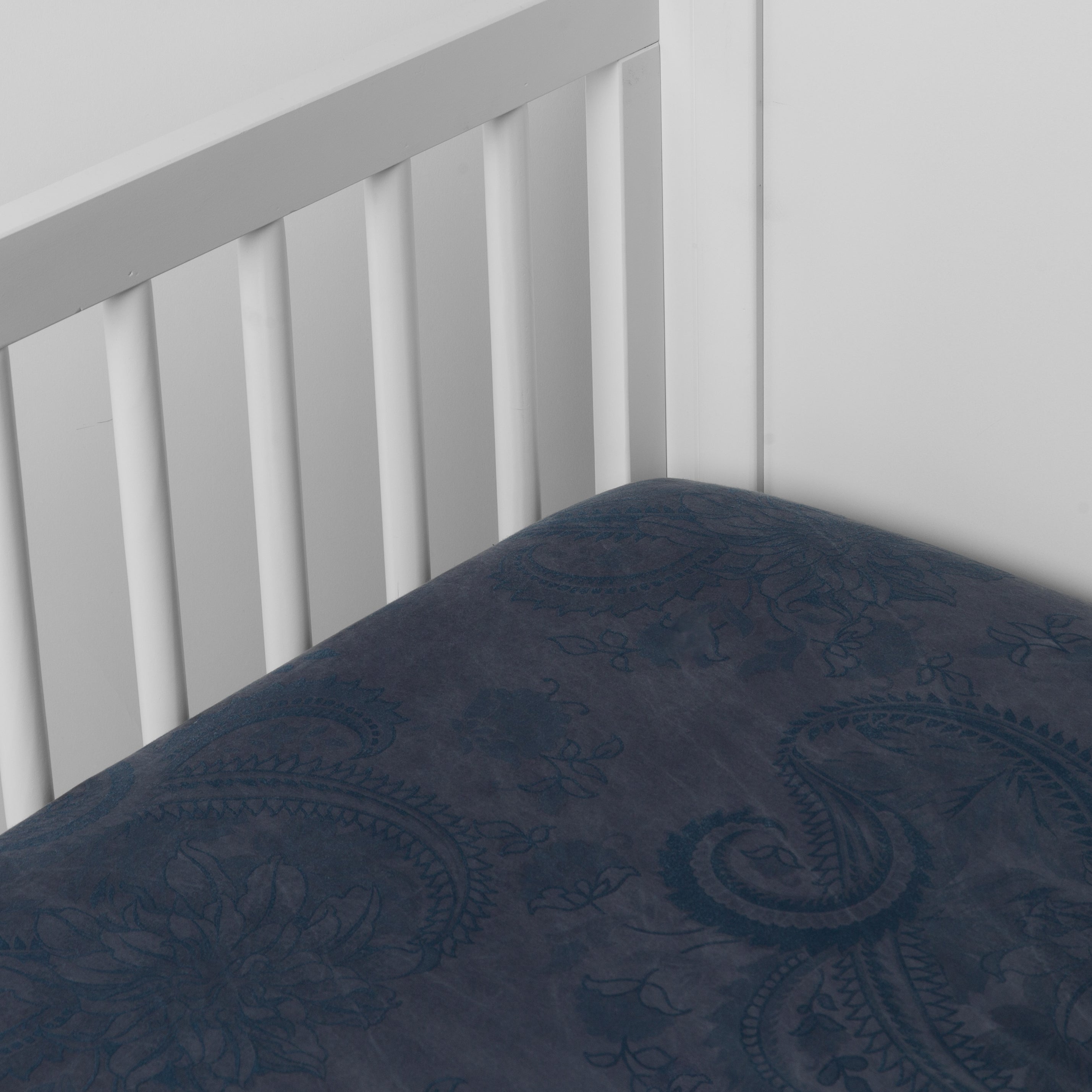 Midnight: silk and tencel™ blend jacquard crib sheet shot from above at a slight angle into the corner of a white crib.