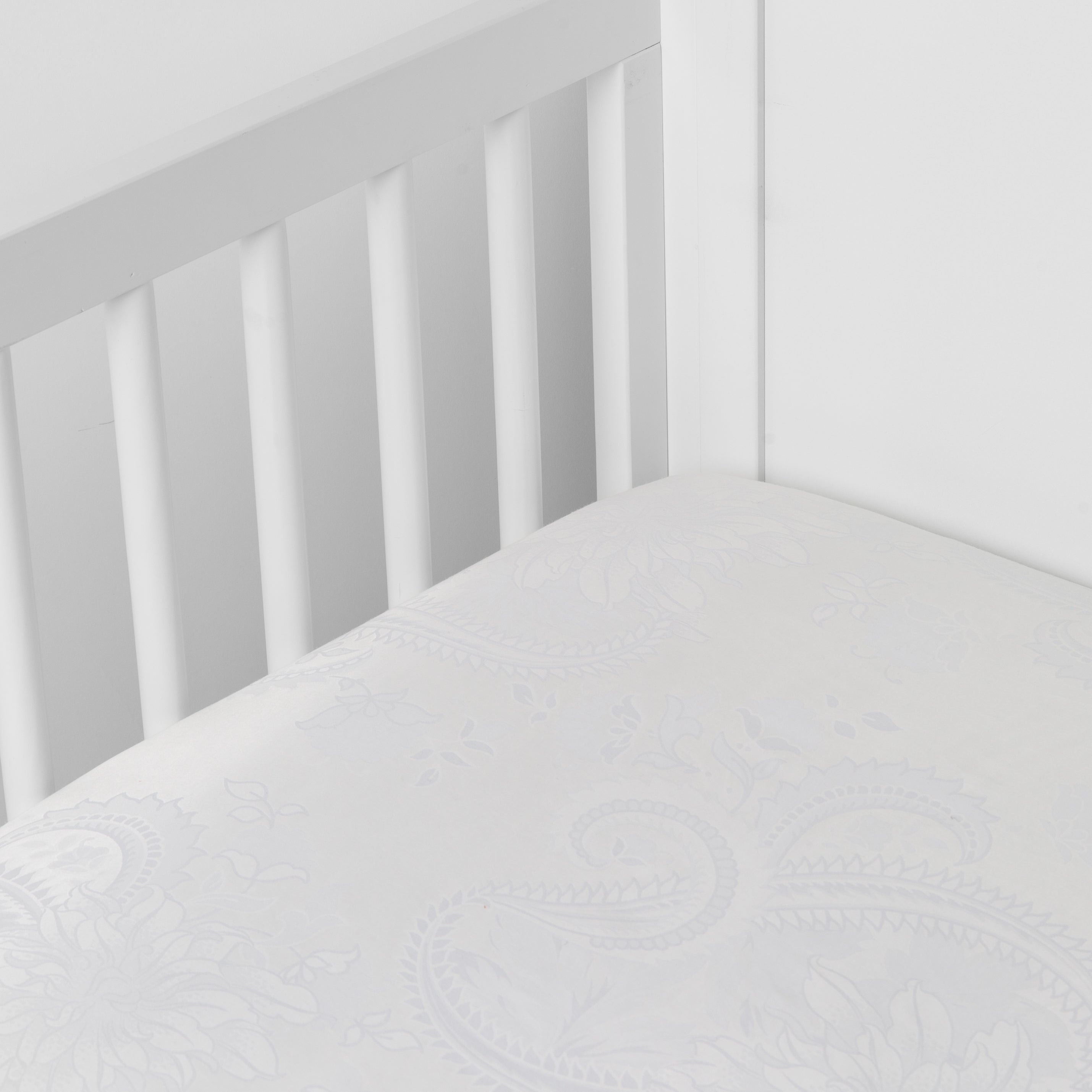 White: a silk and tencel™ crib sheet shown slightly overhread and shot into the corner of a white crib.