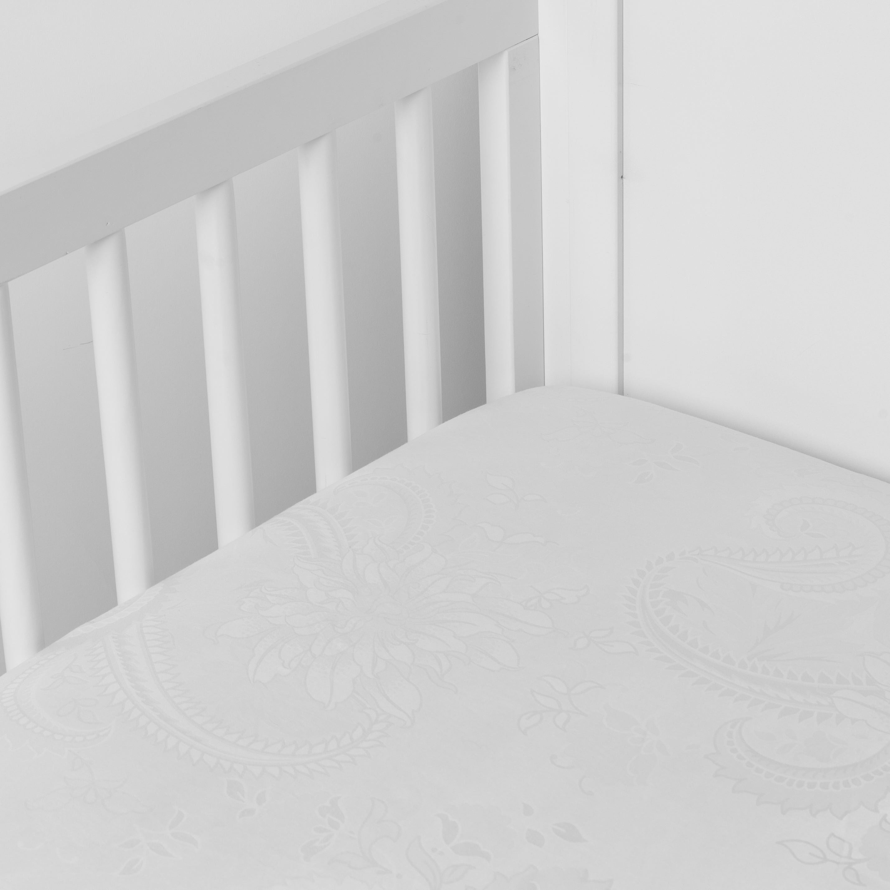 Winter White: silk and tencel™ blend jacquard crib sheet shot from above at a slight angle into the corner of a white crib.