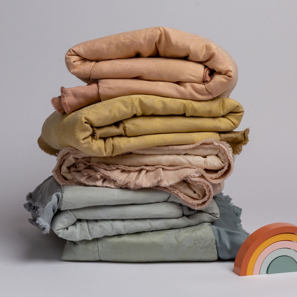 : a stack of silk and tencel™ baby blankets shown in pastel rainbow colors with a set of toy blocks as a rainbow.