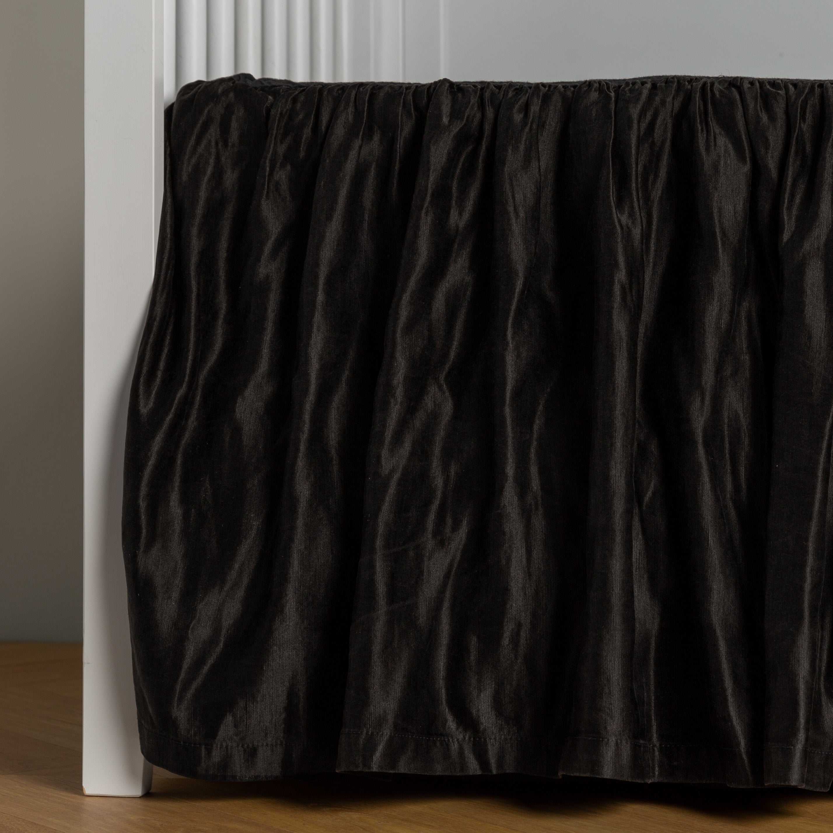 Corvino: charmeuse crib skirt shown on a white crib against a white wall and medium wood floor.