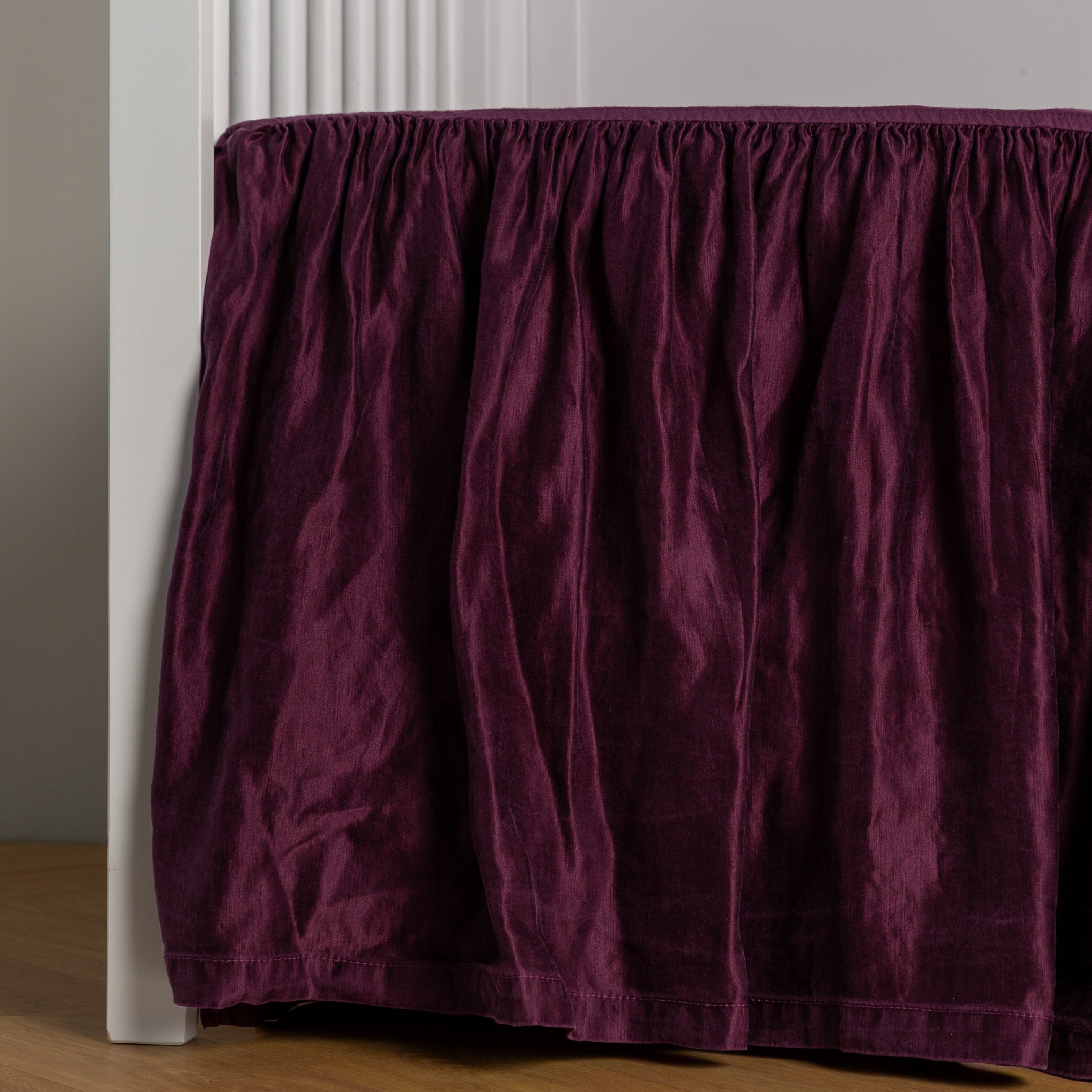 Fig: charmeuse crib skirt shown on a white crib against a white wall and medium wood floor.